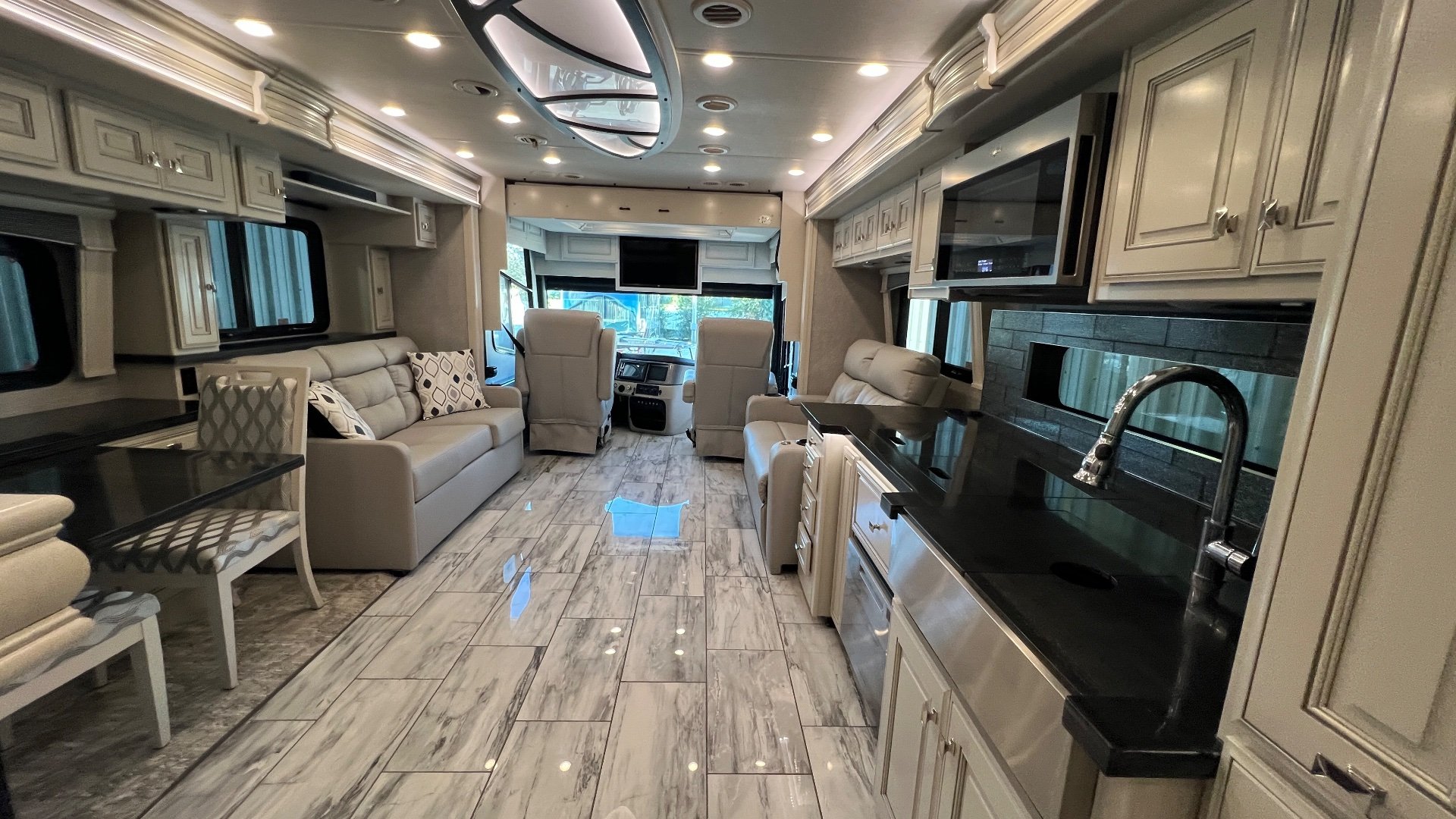 2024 Fleetwood Discovery LXE 40M — Class A lounge with sofas, recliners, entertainment screen, cockpit, and adjacent kitchen sink and cabinetry