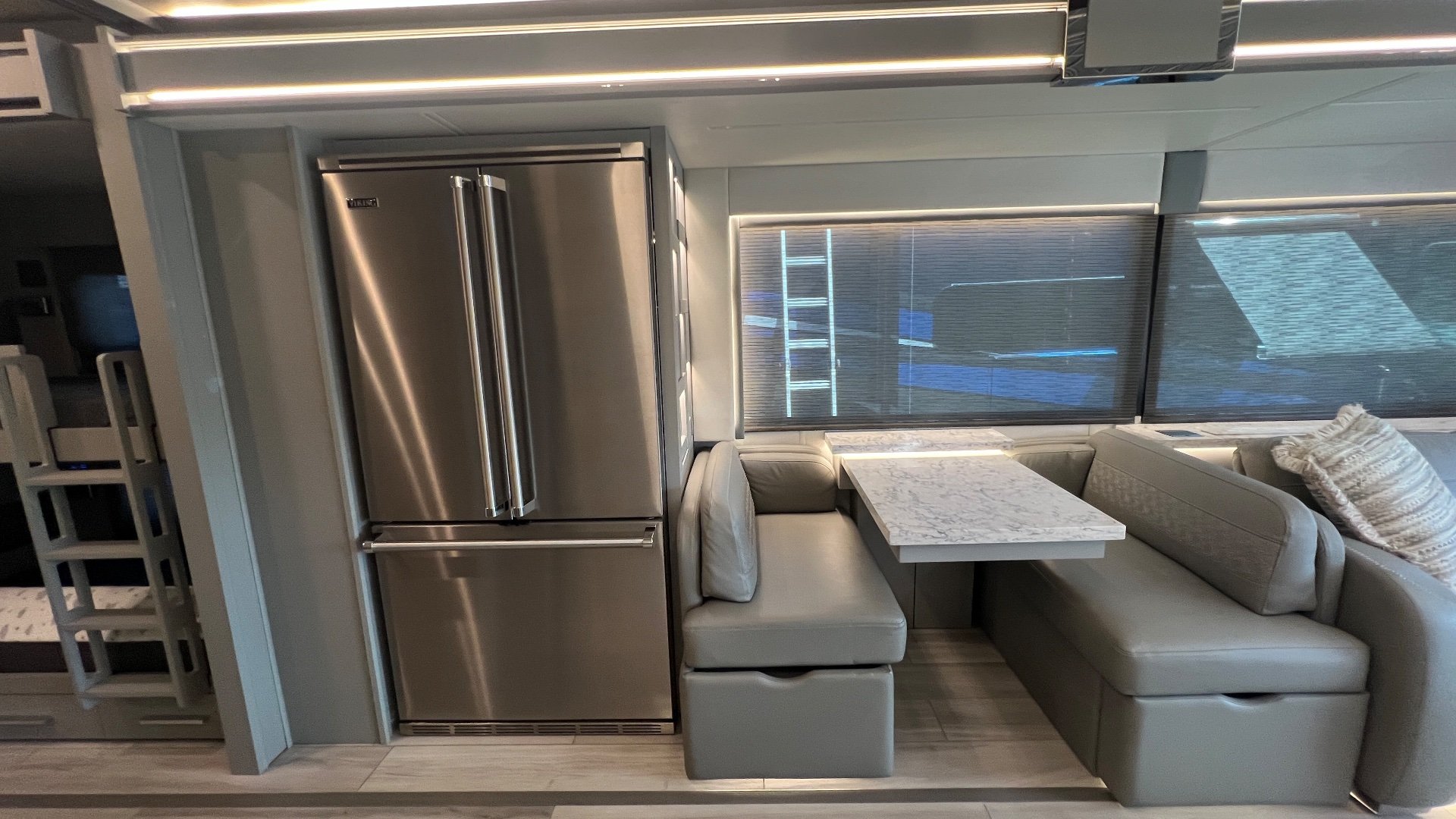 2025 Newmar King Aire 4558 — Dining booth with table beside a stainless refrigerator, with lounge seating and cabinetry visible nearby