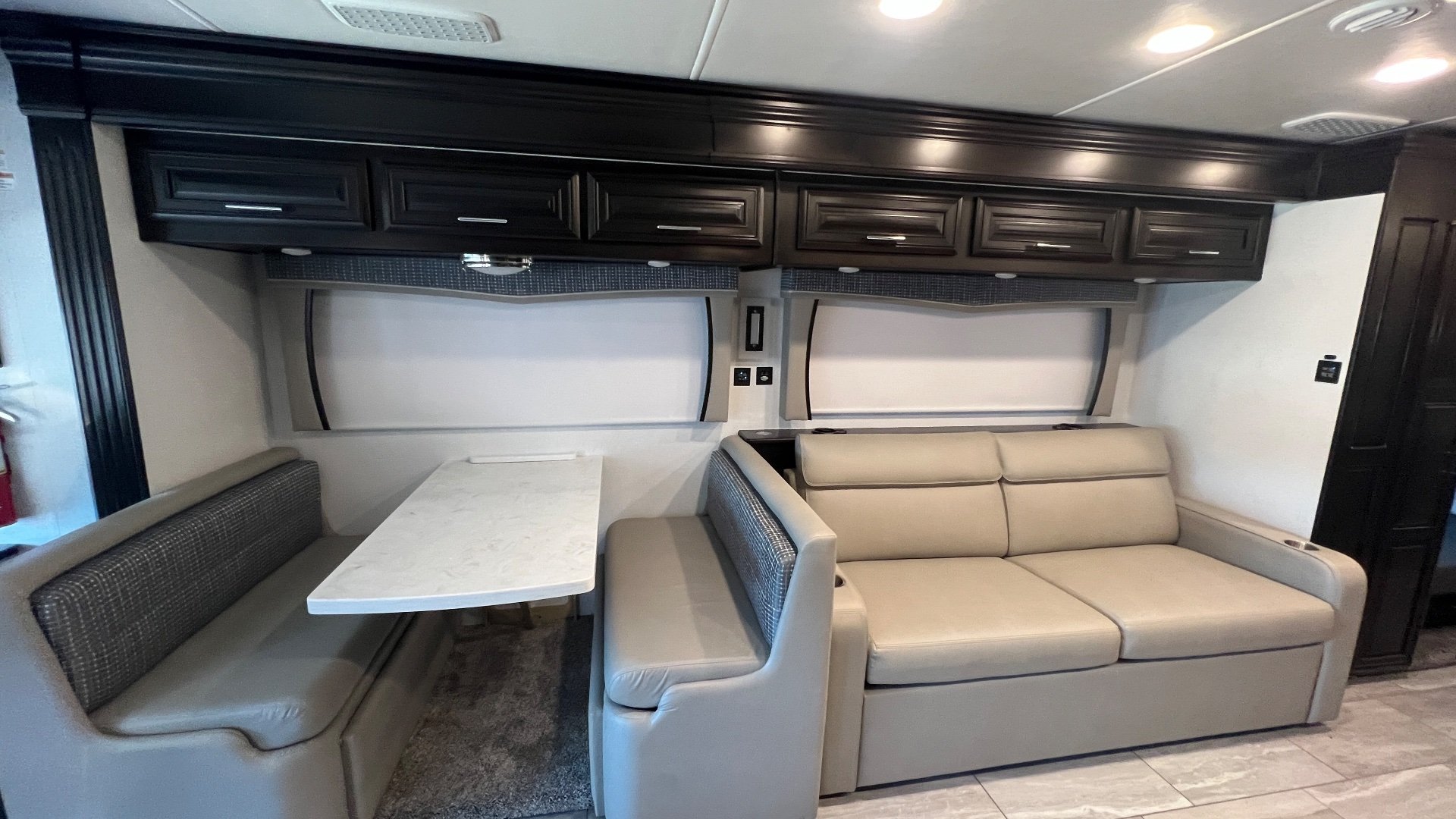 2024 Forest River Berkshire XLT 45CA — Dinette booth with a rectangular tabletop beside a separate sofa and overhead storage cabinets