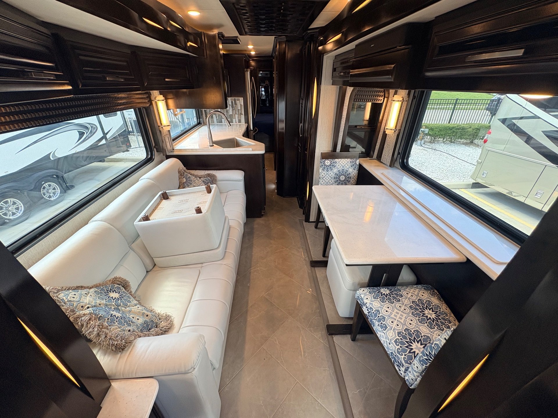 2021 Newmar New Aire 3545 — Class A lounge with a white sofa, adjacent dinette, and kitchen sink and counter along the aisle