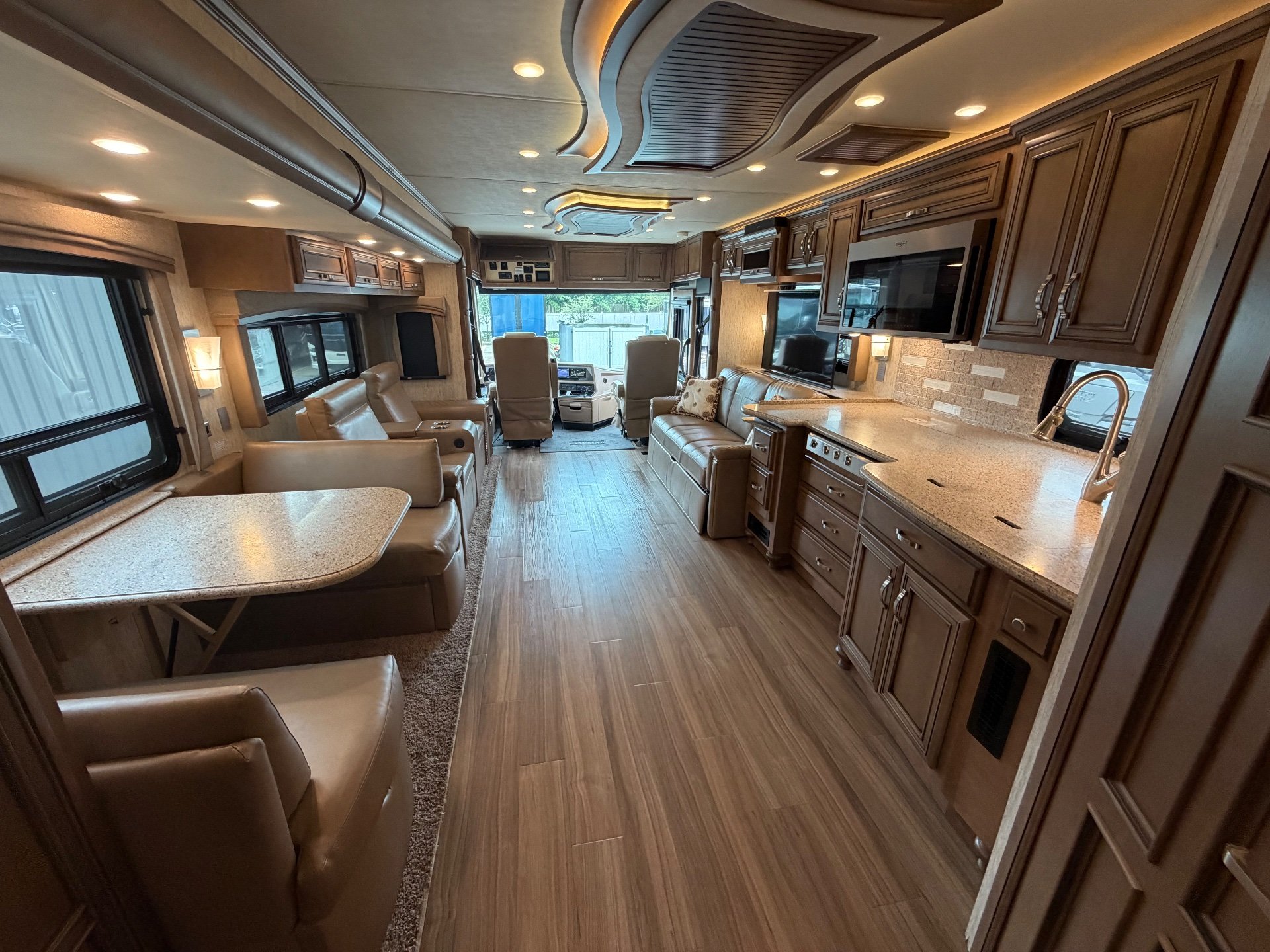 2020 Newmar Kountry Star 4037 — Class A motorhome kitchen with island counter, sink, cabinetry, adjacent sofas, dinette, and cockpit view