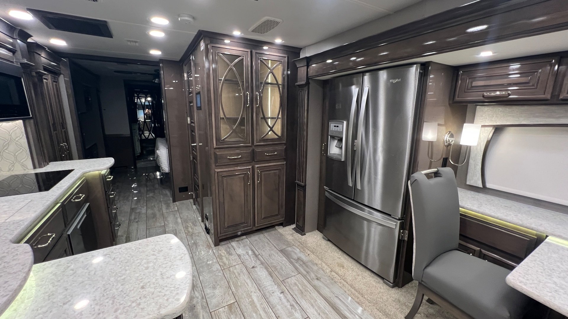 2021 Entegra Coach Cornerstone 45B — Kitchen and dining area with refrigerator, glass-front storage cabinet, island edge, and freestanding chair
