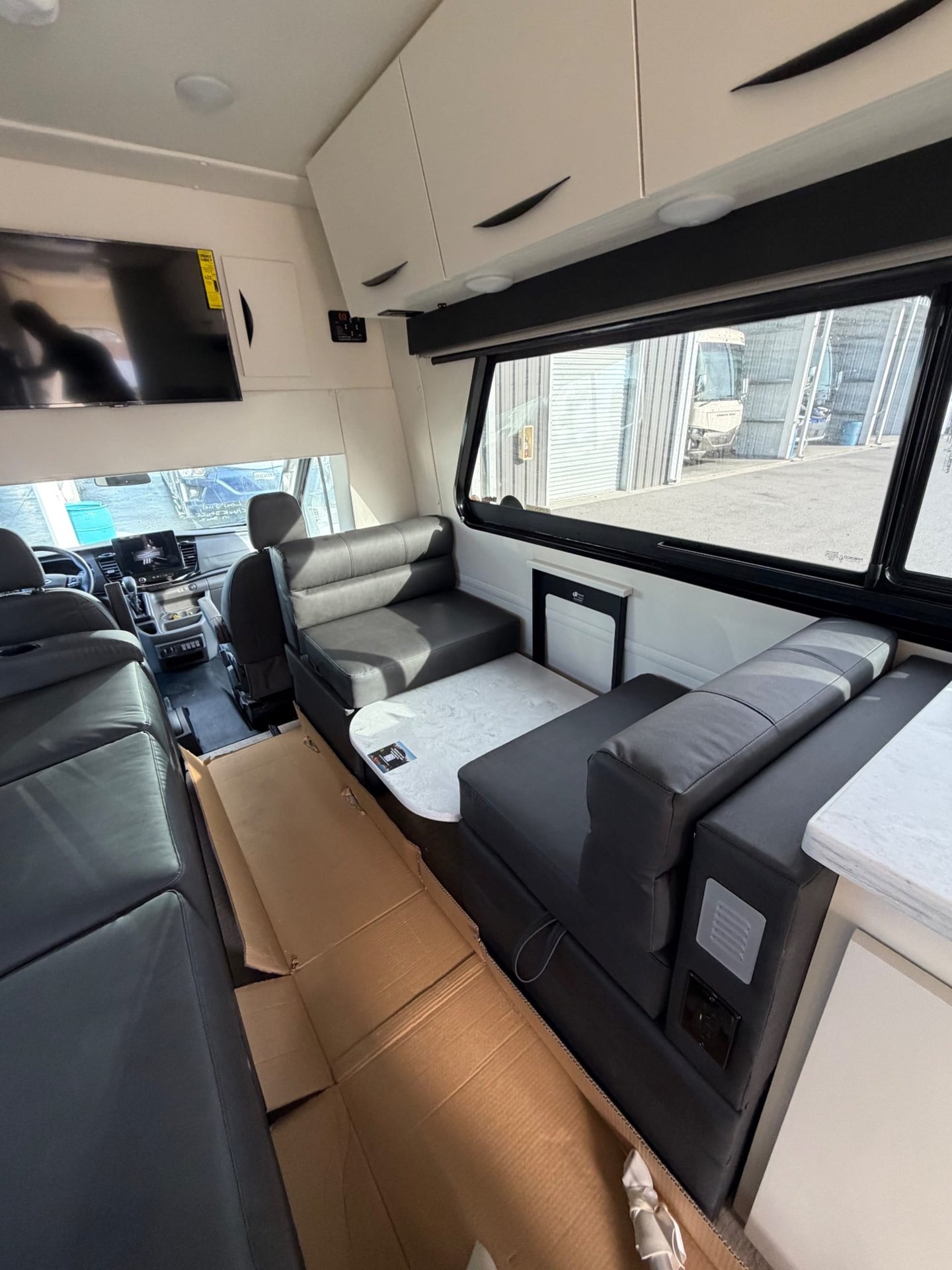 2026 Chinook RV Maverick SS — Rear dinette with opposing benches and table, alongside a long lounge sofa and visible cockpit