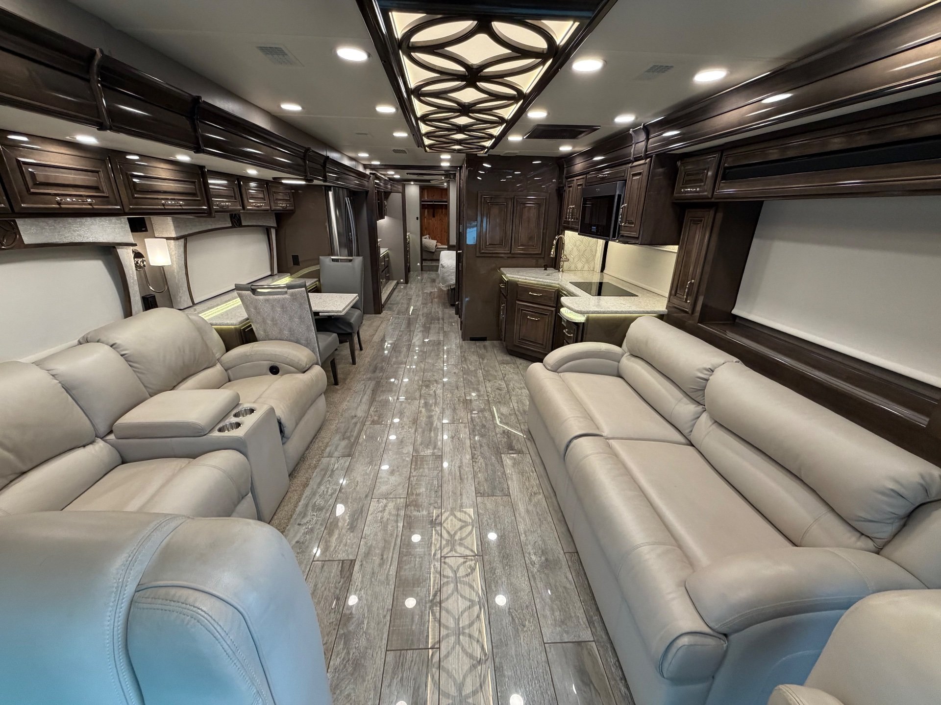 2021 Entegra Coach Cornerstone 45F — Class A motorhome lounge with opposing sofas, a dinette, and rear kitchen cabinetry along a central aisle