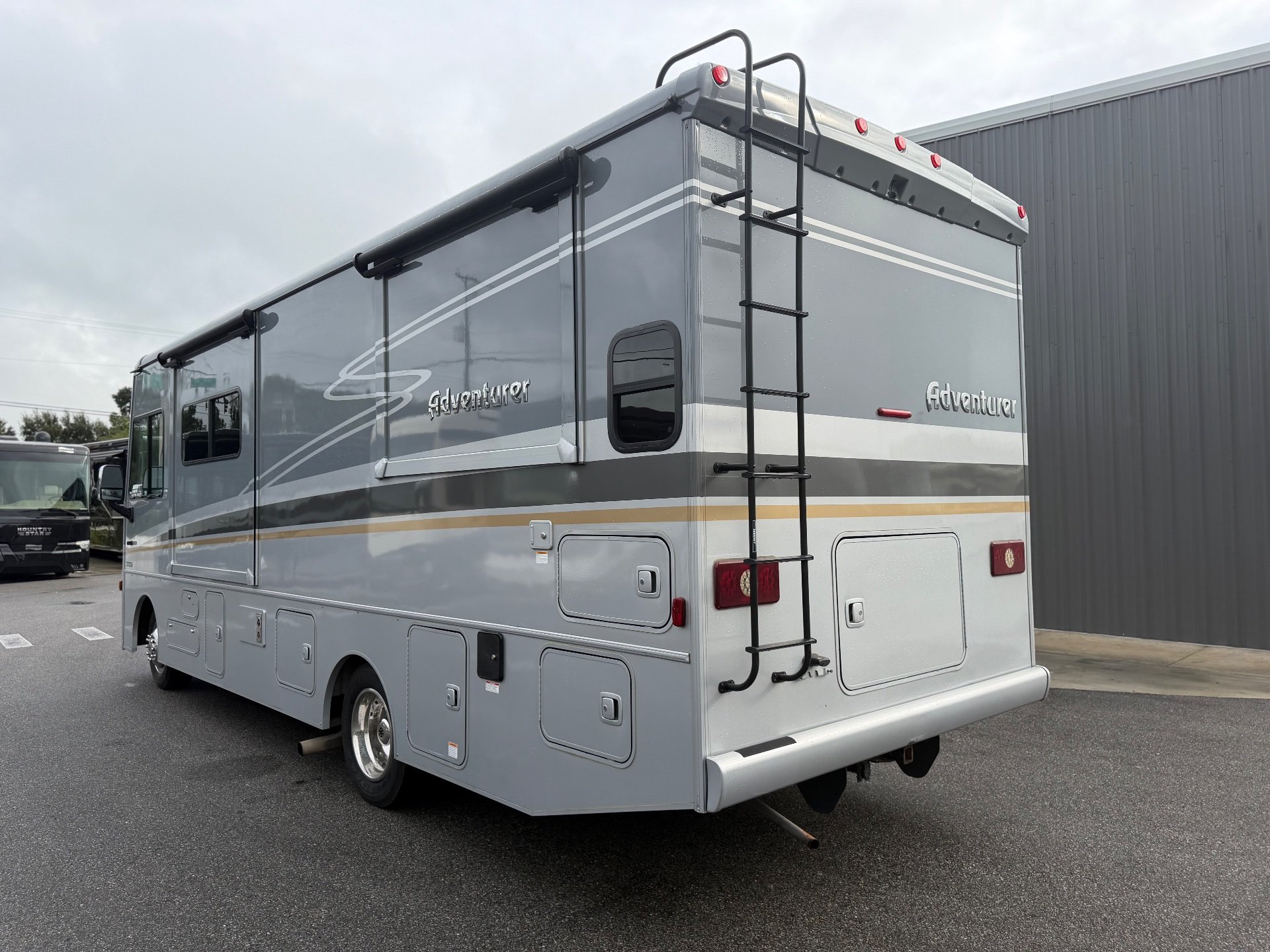 2021 Winnebago Adventurer 27N — The motorhome's rear and side exterior with ladder, lights, body panels, and storage doors