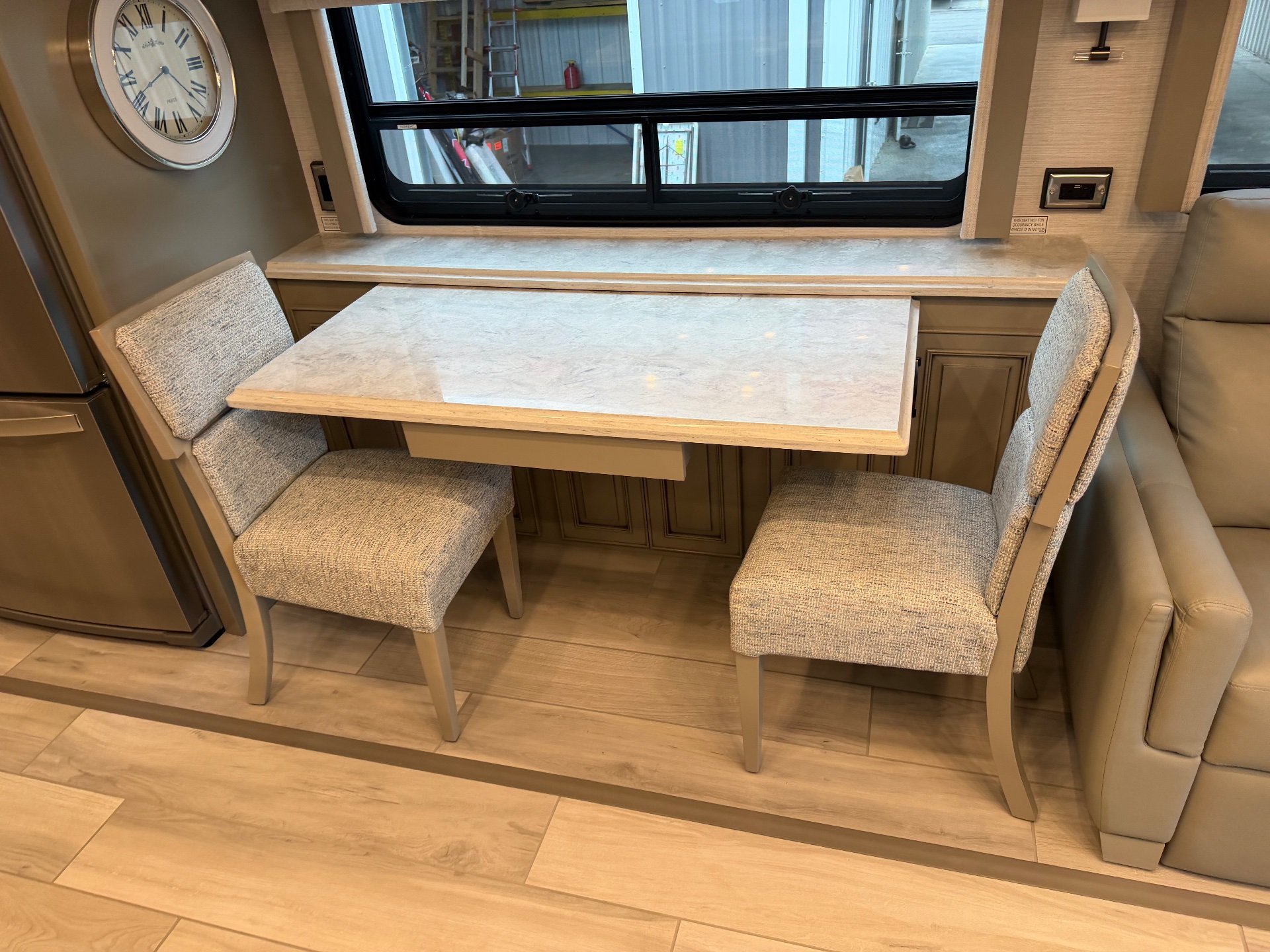 2025 Newmar Dutch Star 4369 — Dining table with two chairs beside a living recliner and refrigerator at the kitchen edge