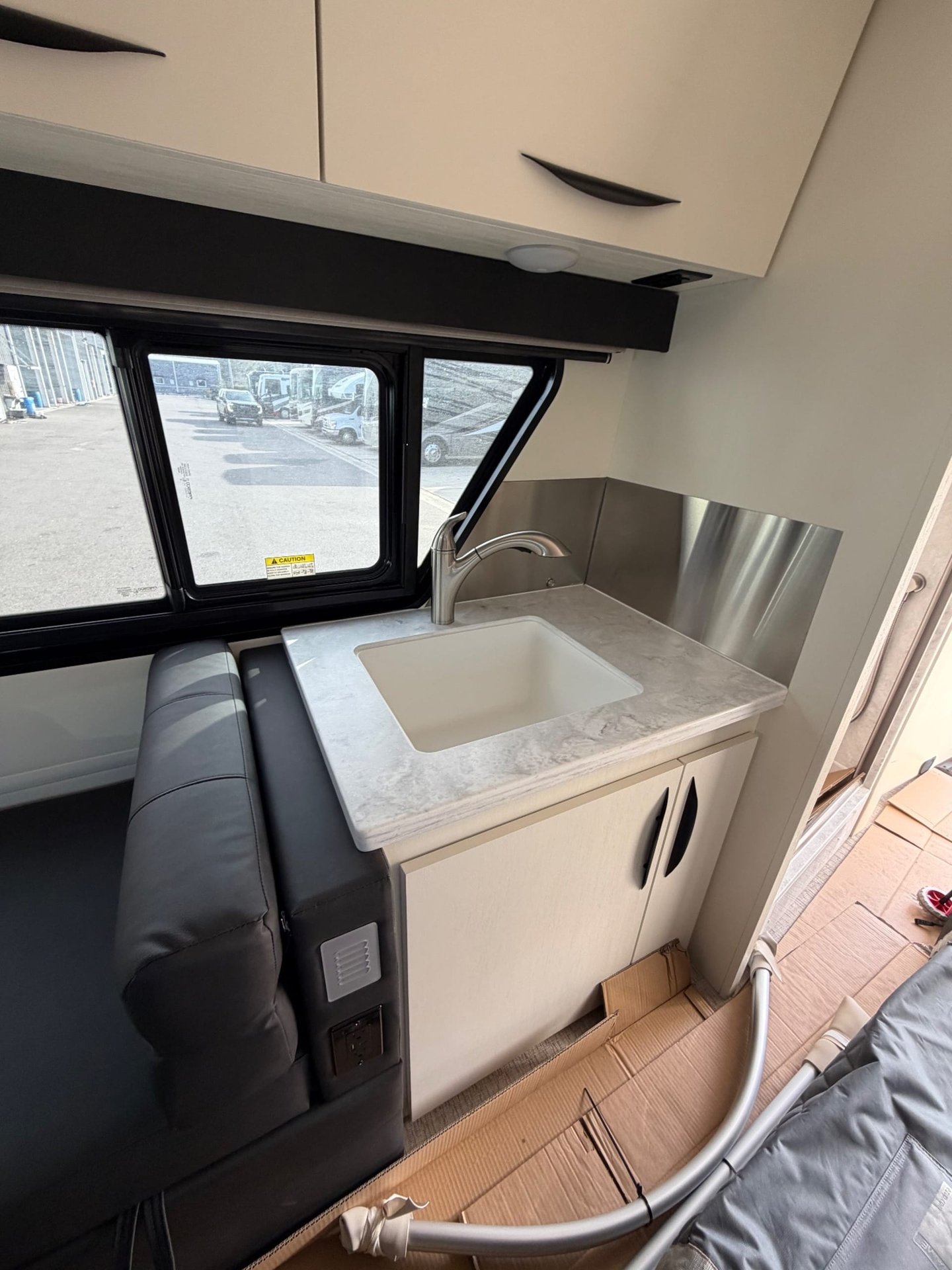 2026 Chinook RV Maverick SS — Van kitchen sink with curved faucet, countertop, backsplash, overhead cabinets, and adjacent upholstered seating
