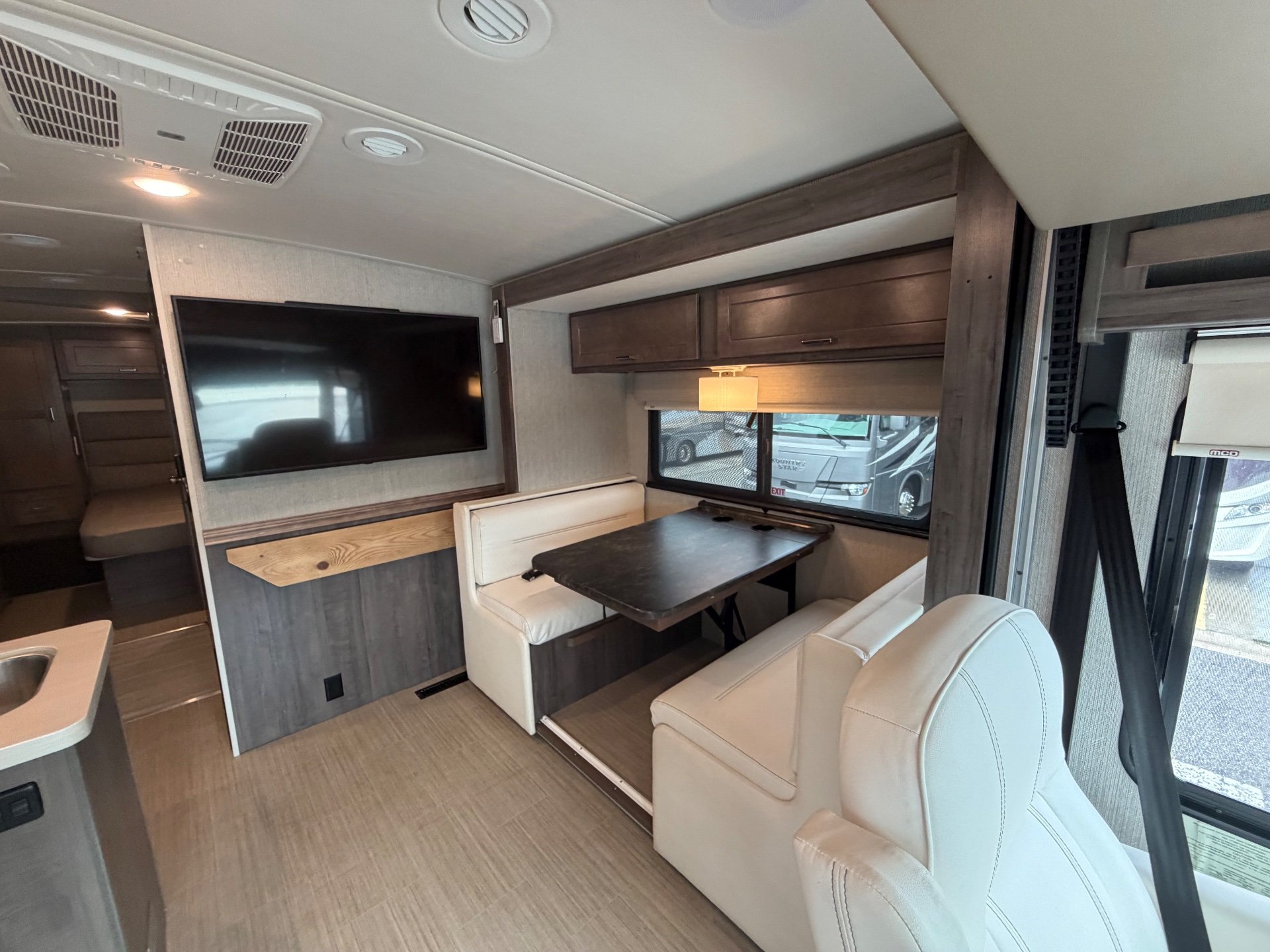 2021 Winnebago Adventurer 27N — Dinette with facing upholstered benches beside the television and front captain’s chair
