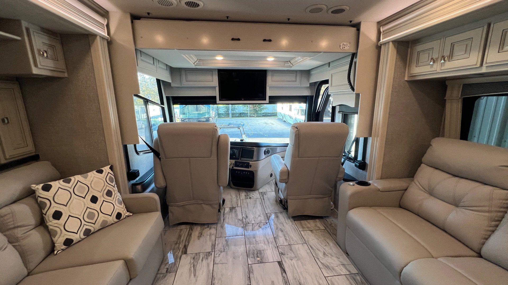 2024 Fleetwood Discovery LXE 40M — Class A cockpit with dashboard and captain chairs viewed from the lounge, with sofas framing the aisle