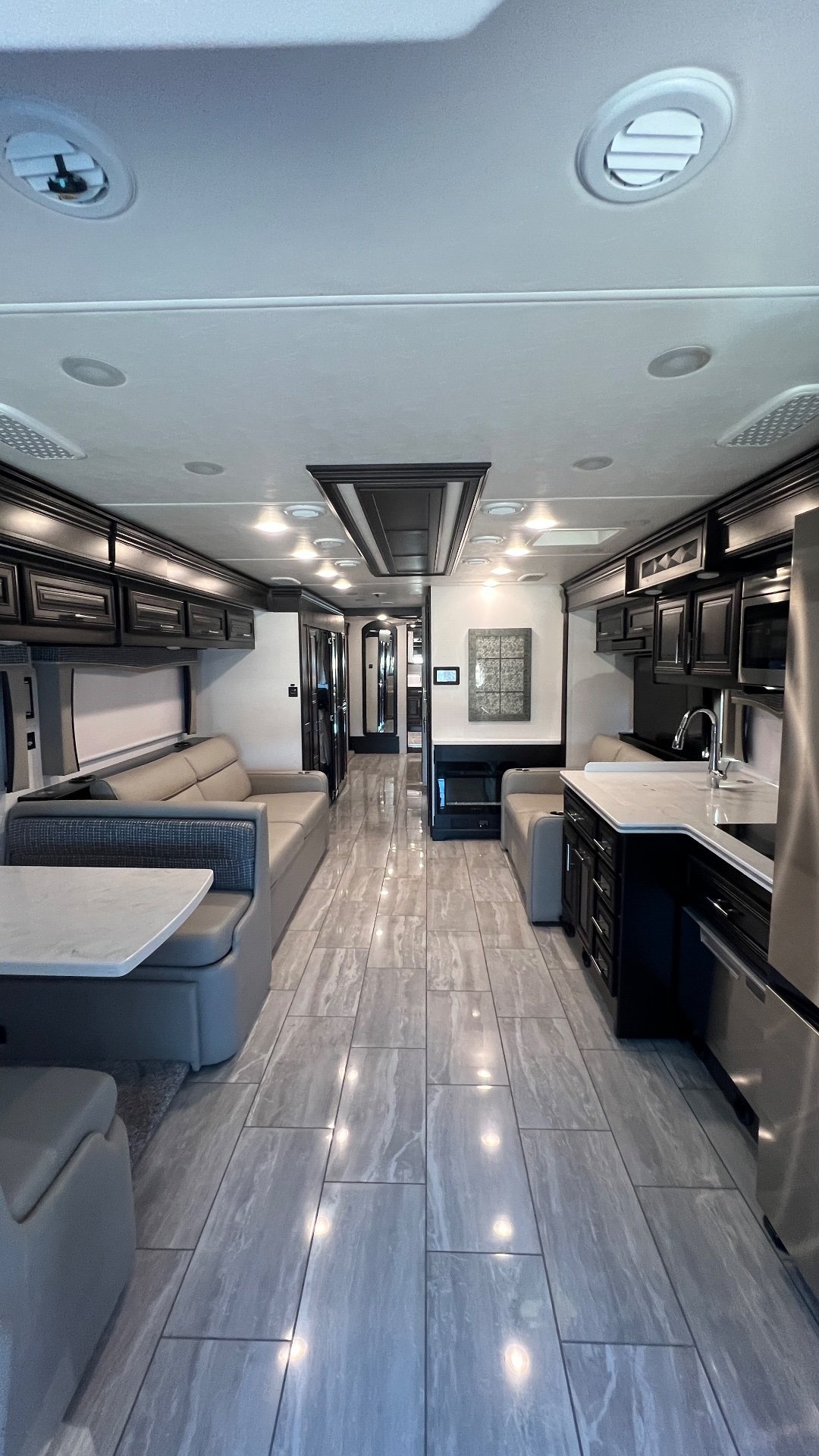 2024 Forest River Berkshire XLT 45CA — Class A lounge with sofas, entertainment seating, kitchen counters, sink, and cabinetry along a tiled central aisle