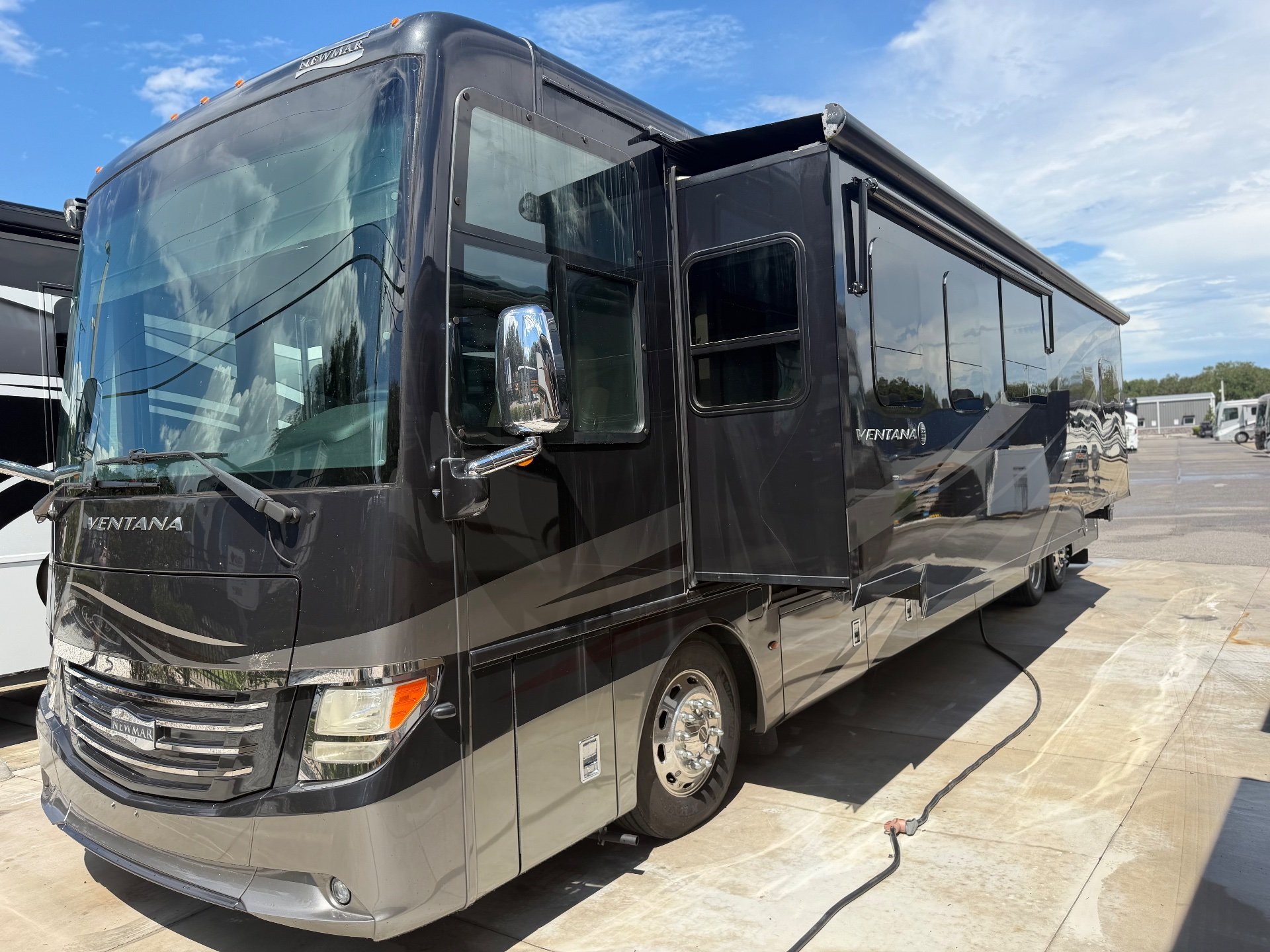2018 Newmar Ventana 4369 — Front-side exterior photograph visibly shows the coach shell, windshield, entry area, wheel, awning, and extended slide-out