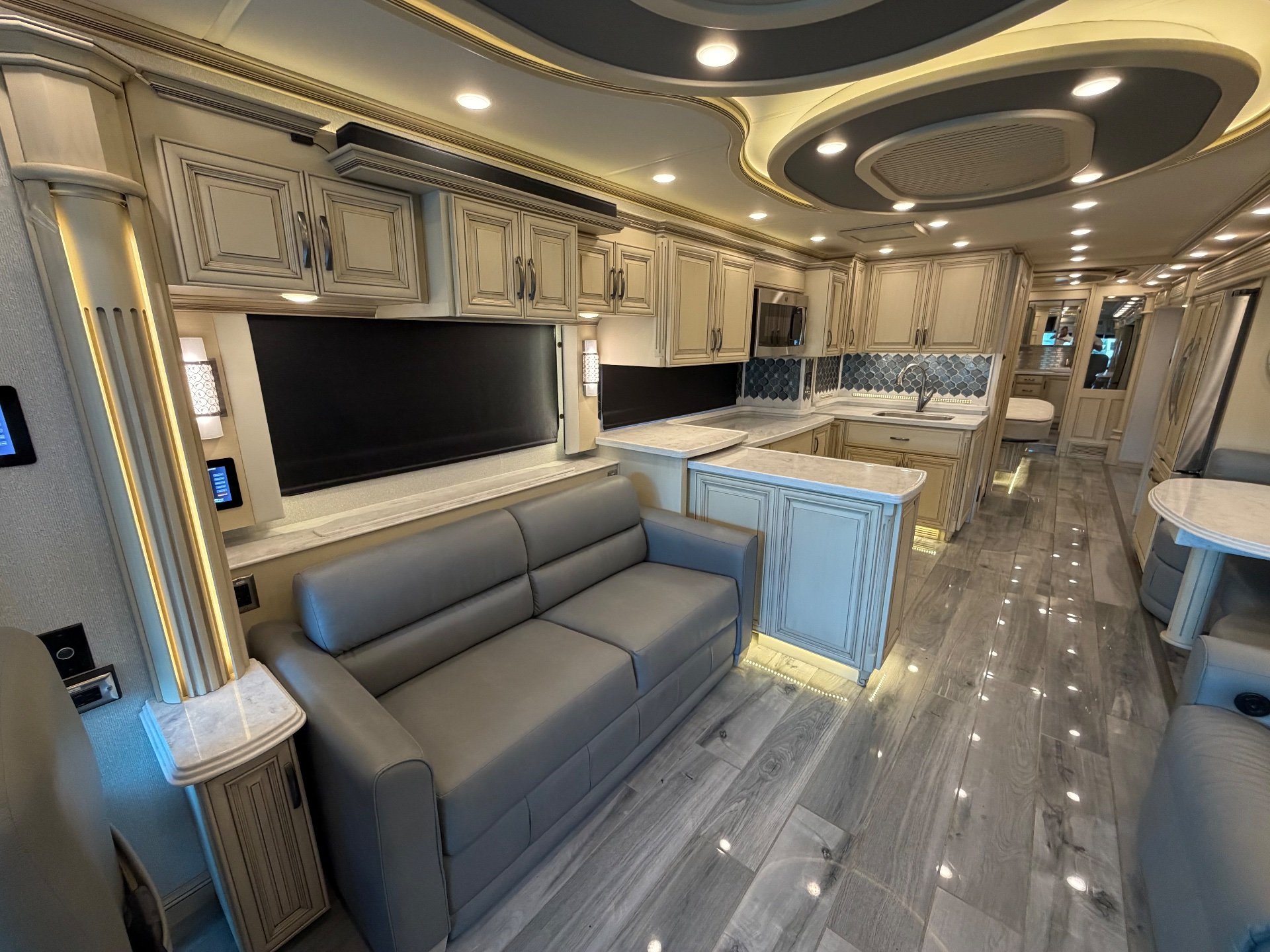2022 Newmar Essex 4569 — Motorhome kitchen with island, sink, backsplash, and cabinetry opening toward the lounge and rear dinette