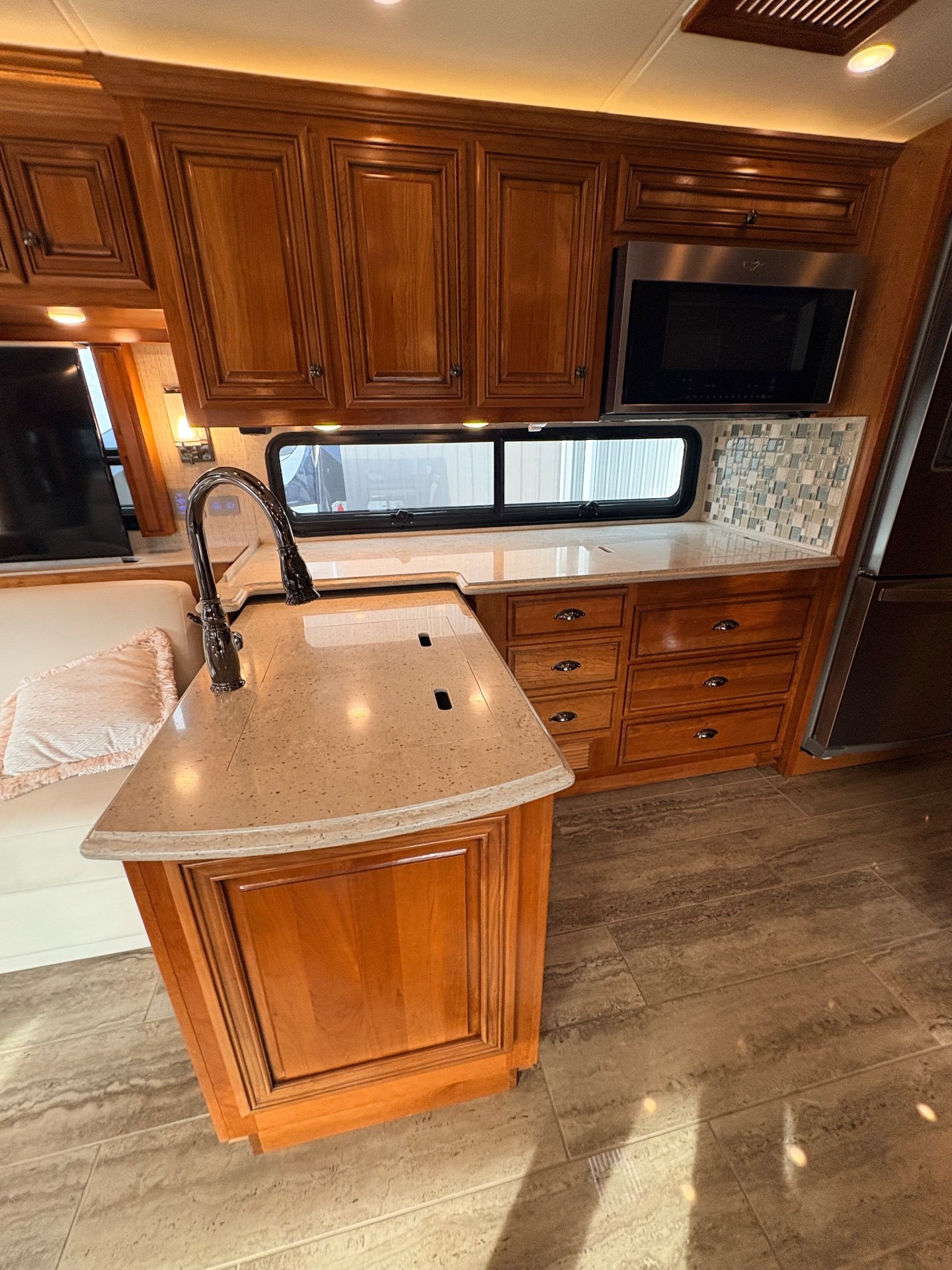 2020 Newmar Dutch Star 3717 — Kitchen island with sink and tall faucet faces counters, drawers, mosaic backsplash, microwave, and refrigerator beside a sofa