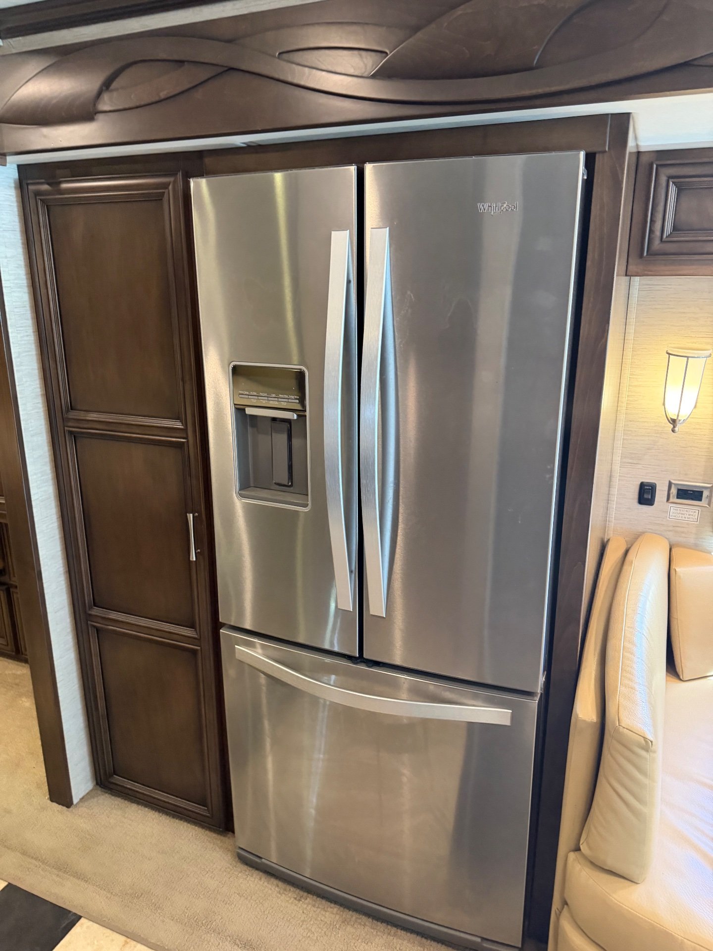 2018 Newmar Ventana 4369 — Stainless-steel refrigerator with water dispenser beside tall dark wood kitchen cabinetry