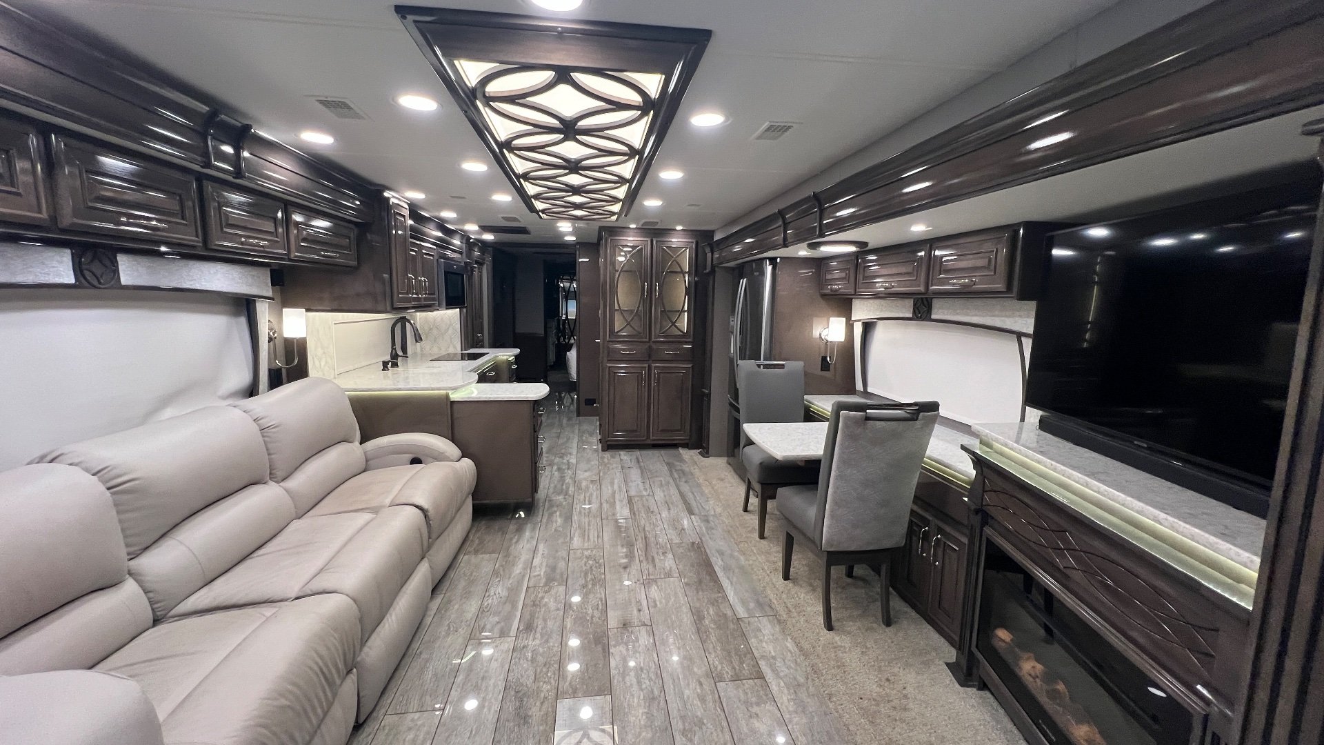 2021 Entegra Coach Cornerstone 45B — Motorhome interior overview with sofa, kitchen island, dining table, cabinetry, fireplace, and television