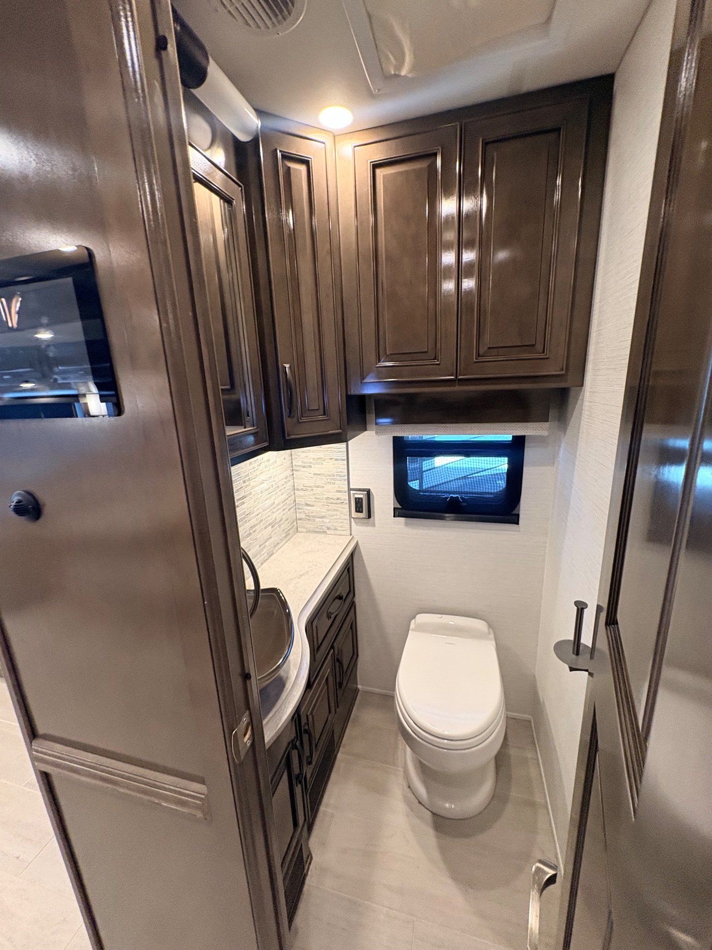 2025 Newmar Dutch Star 4369 — Bathroom with toilet, corner vanity, mirrored cabinetry, window, and overhead storage