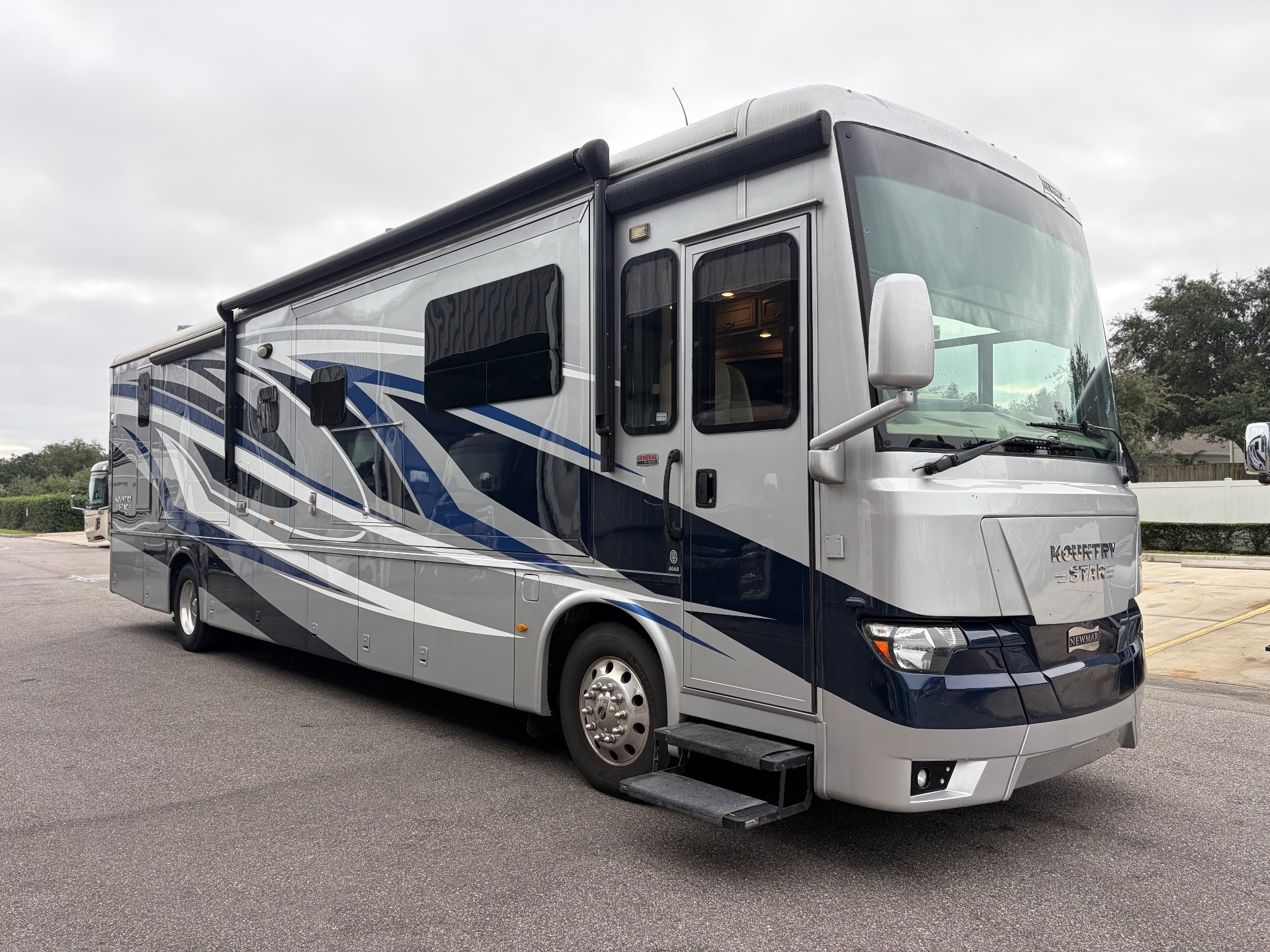2023 Newmar Kountry Star 4068 — Photo visibly shows the outside front and side of a Kountry Star motorhome, including body, wheel, awning, and entry steps