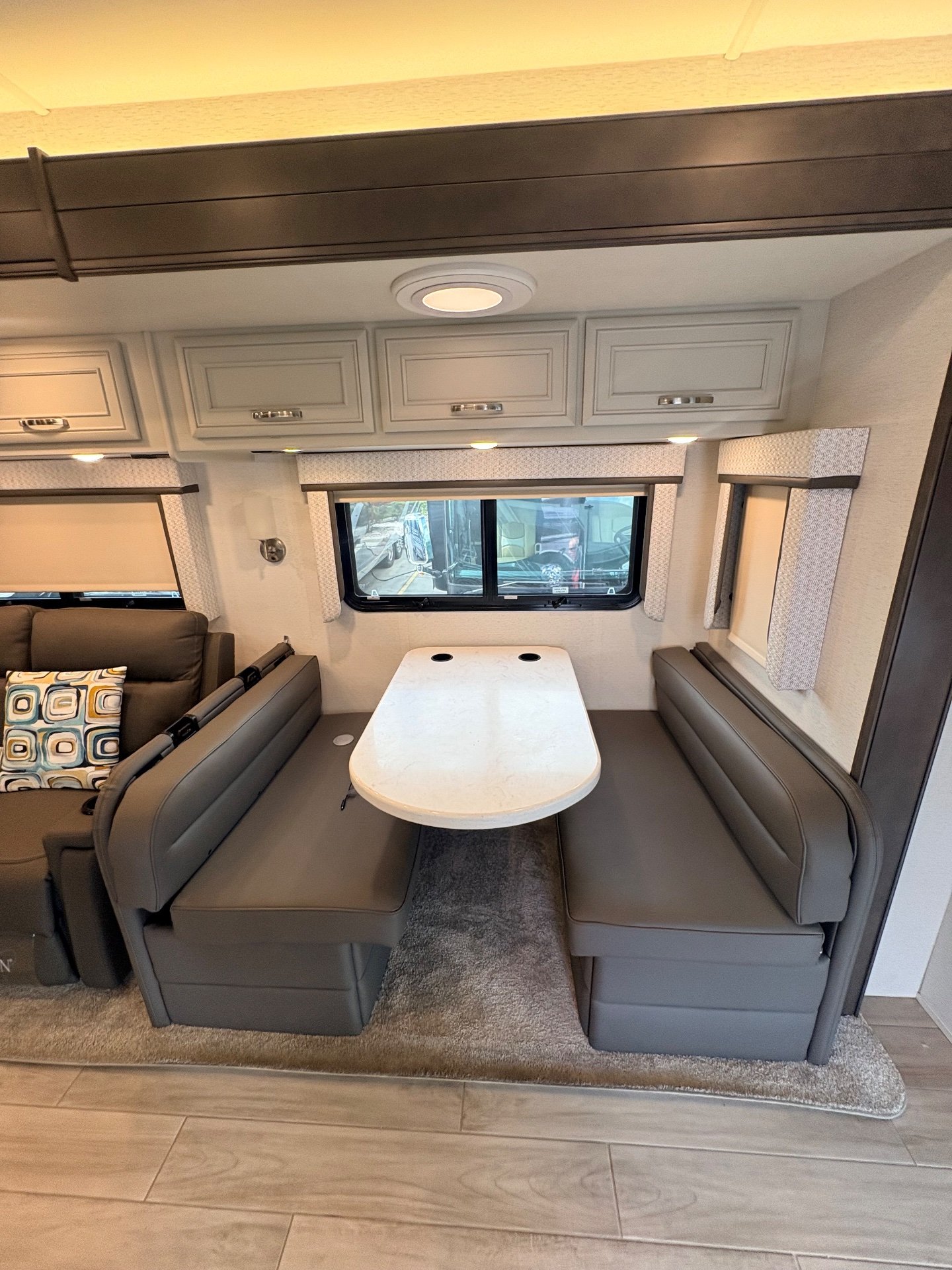 2025 Entegra Coach Accolade XL 37L — Motorhome dinette with opposing upholstered benches, rounded table, windows, and overhead storage cabinets