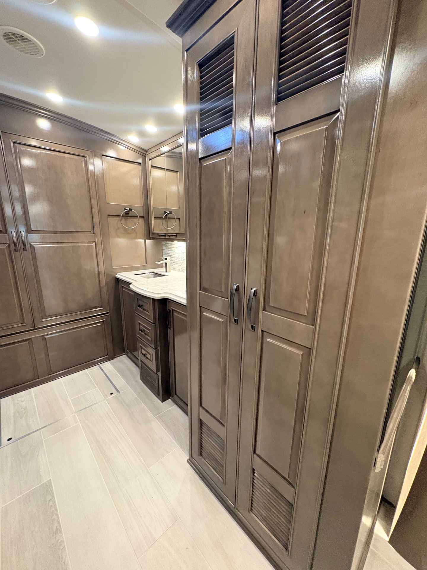 2025 Newmar Dutch Star 4369 — Bathroom corridor with a vanity sink, mirrored cabinet, towel rings, and tall louvered storage doors