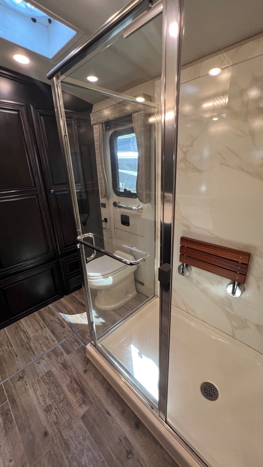 2018 Newmar Dutch Star 4369 — Motorhome bathroom shower enclosure beside a toilet, with a window, grab rails, and marble-patterned wall panels