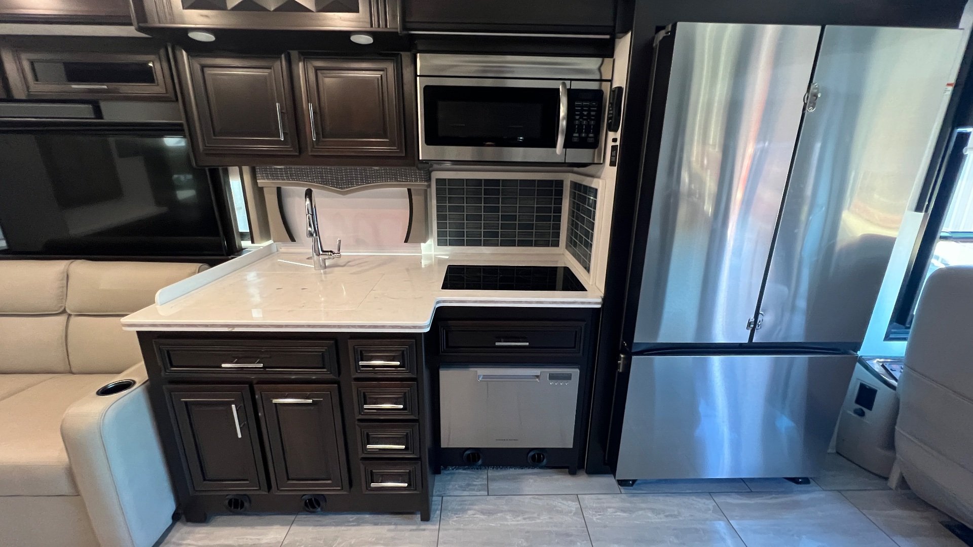 2024 Forest River Berkshire XLT 45CA — Kitchen with sink, microwave, cooktop, dishwasher, cabinetry, and refrigerator beside a lounge loveseat