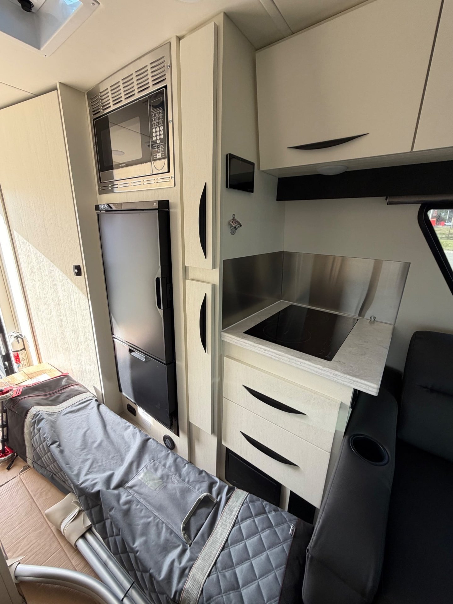 2026 Chinook RV Maverick SS — Van galley with induction cooktop, refrigerator, microwave, drawers, and a nearby covered sleeping surface