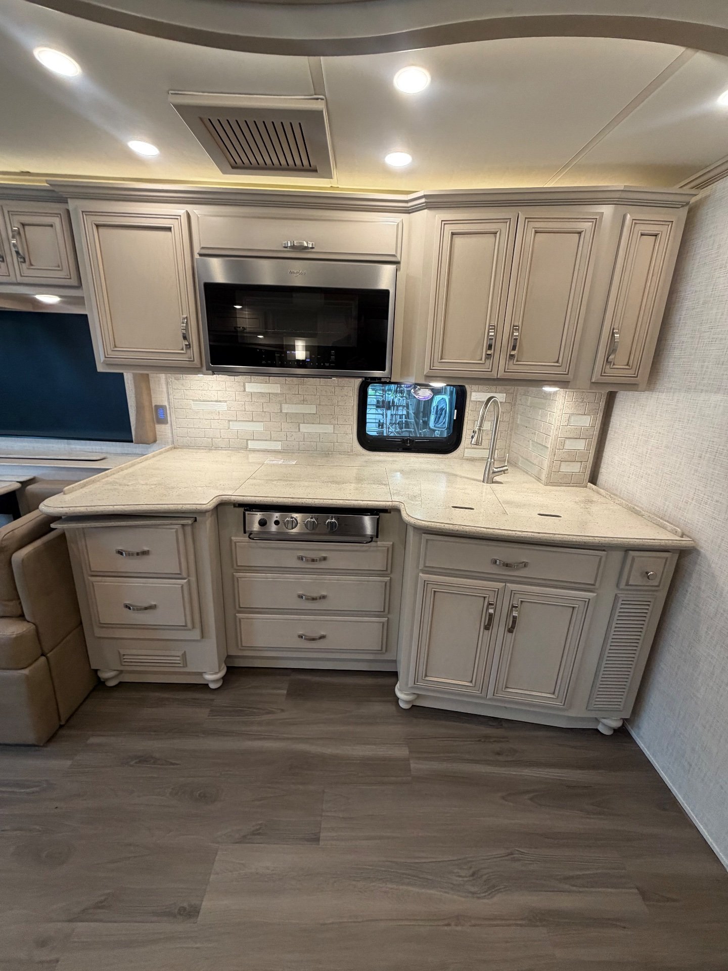2023 Newmar Kountry Star 4068 — Motorhome kitchen with countertop, sink, cooktop, microwave, backsplash, and extensive overhead cabinetry