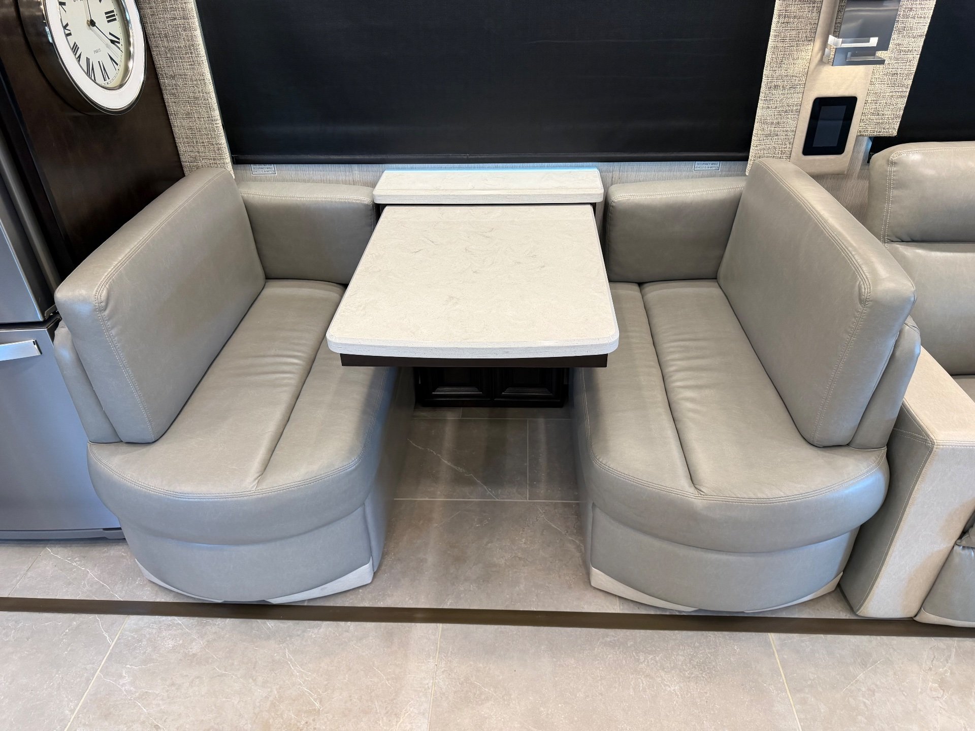 2023 Newmar Supreme Aire 4575 — U-shaped dining booth with upholstered benches and a rectangular tabletop beneath a window shade