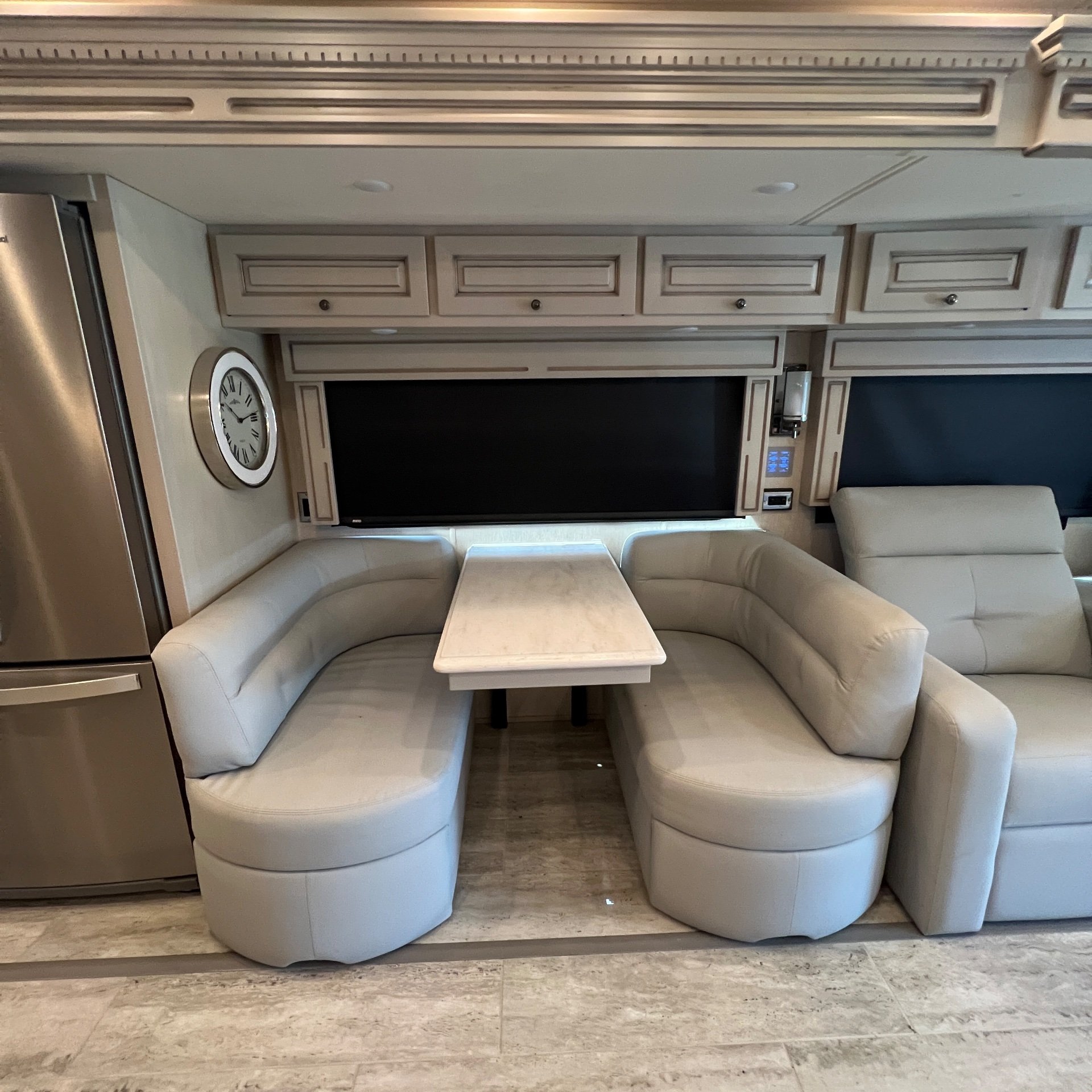 2022 Newmar Dutch Star 4081 — U-shaped dinette with freestanding table beside a recliner, refrigerator, window, and overhead storage