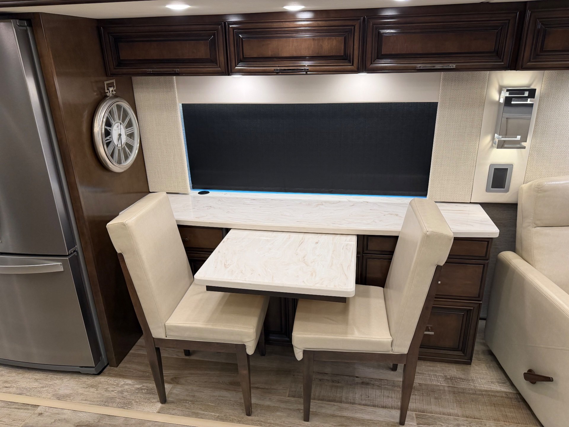 2020 Newmar Mountain Aire 4551 — Freestanding dining table and two chairs sit beside a refrigerator, cabinetry, and a nearby recliner