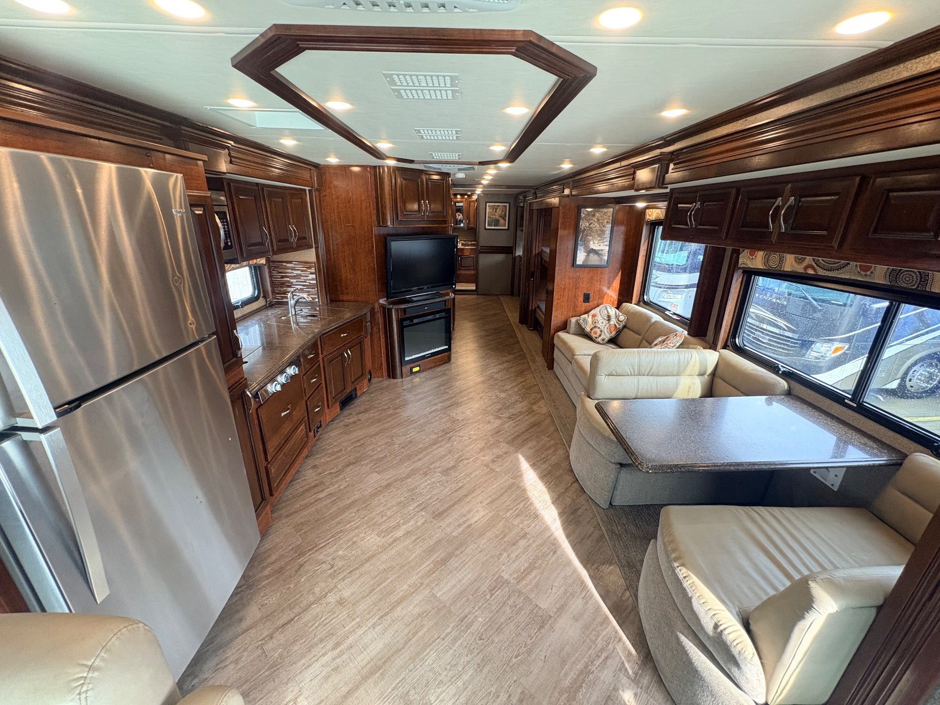 2019 Fleetwood Pace Arrow LXE 38N — Class A motorhome overview showing refrigerator and kitchen cabinetry beside a central aisle, television, and dinette seating