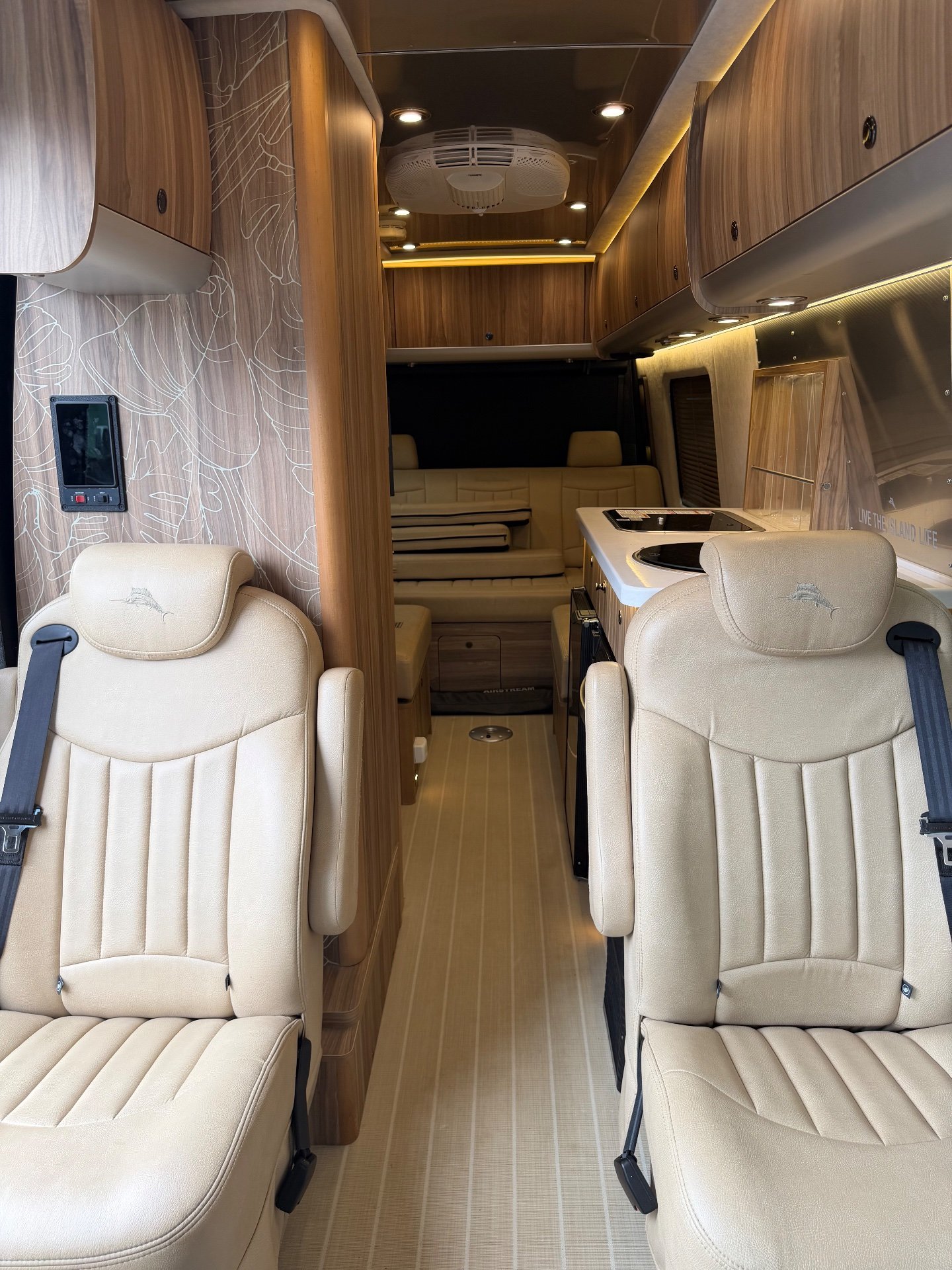 2020 Airstream Interstate 24GL 4WD — Class B van interior shows front captain’s chairs, a rear lounge bench, and galley cabinetry with covered cooktops