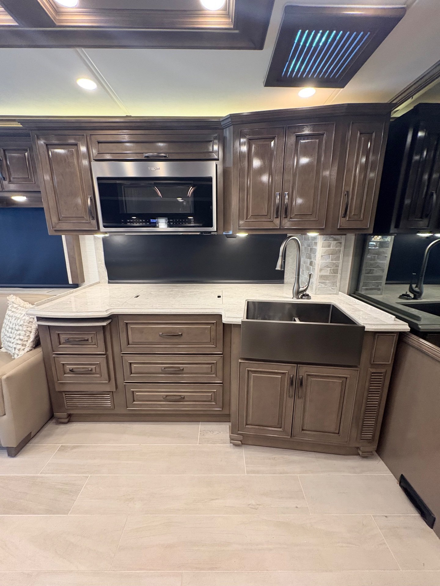 2025 Newmar Dutch Star 4369 — Motorhome kitchen with farmhouse sink, curved faucet, microwave, countertop, backsplash, and dark wood cabinets