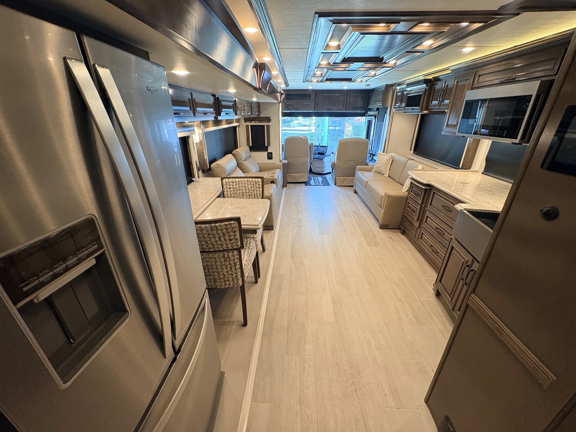 2025 Newmar Dutch Star 4369 — Class A motorhome interior overview with refrigerator and kitchen counters beside dining seating, sofas, and cockpit seats