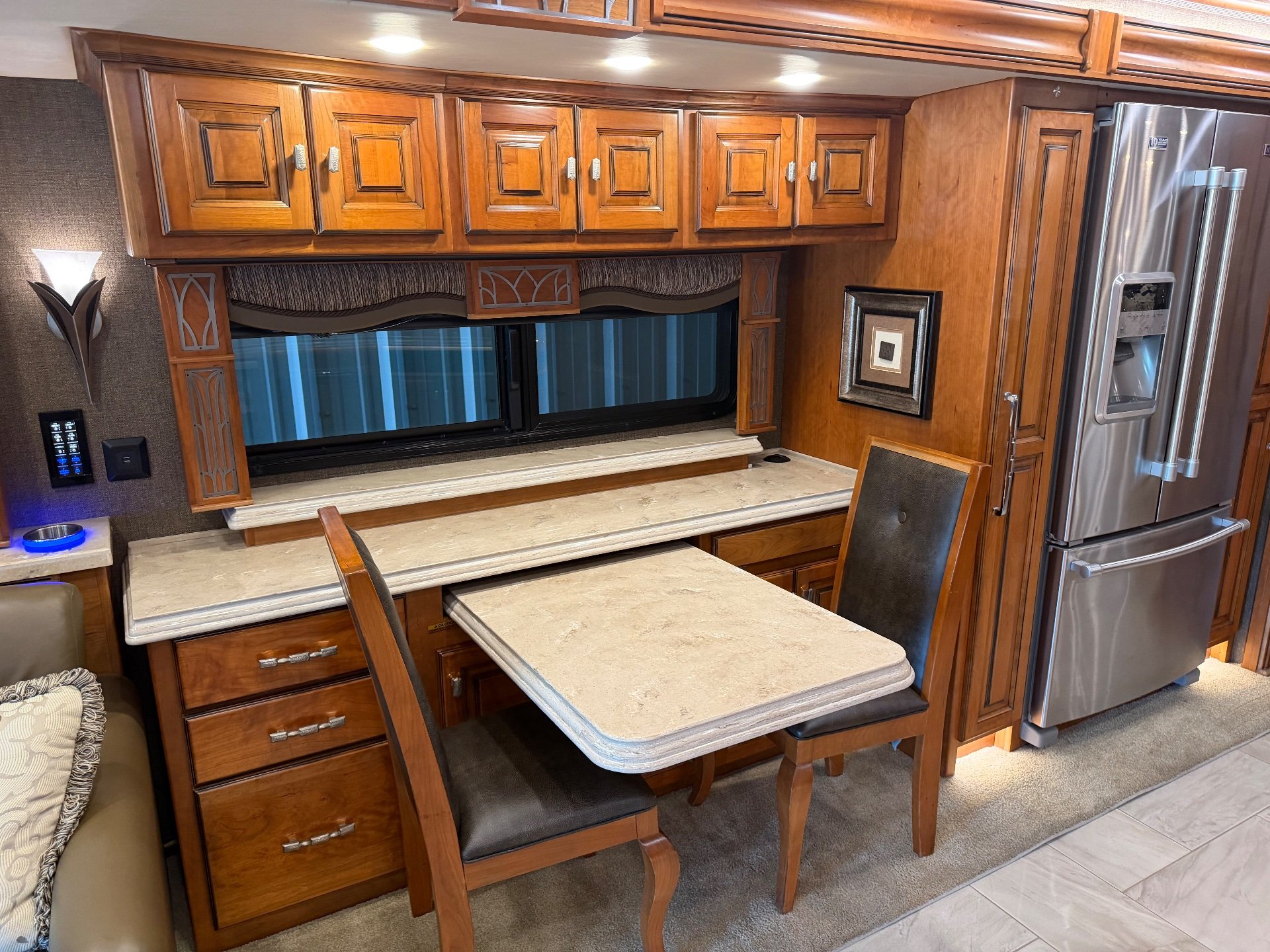 2017 Tiffin Allegro Bus 45 OPP — Freestanding dining table and chairs beside a kitchen counter, refrigerator, drawers, and overhead cabinets