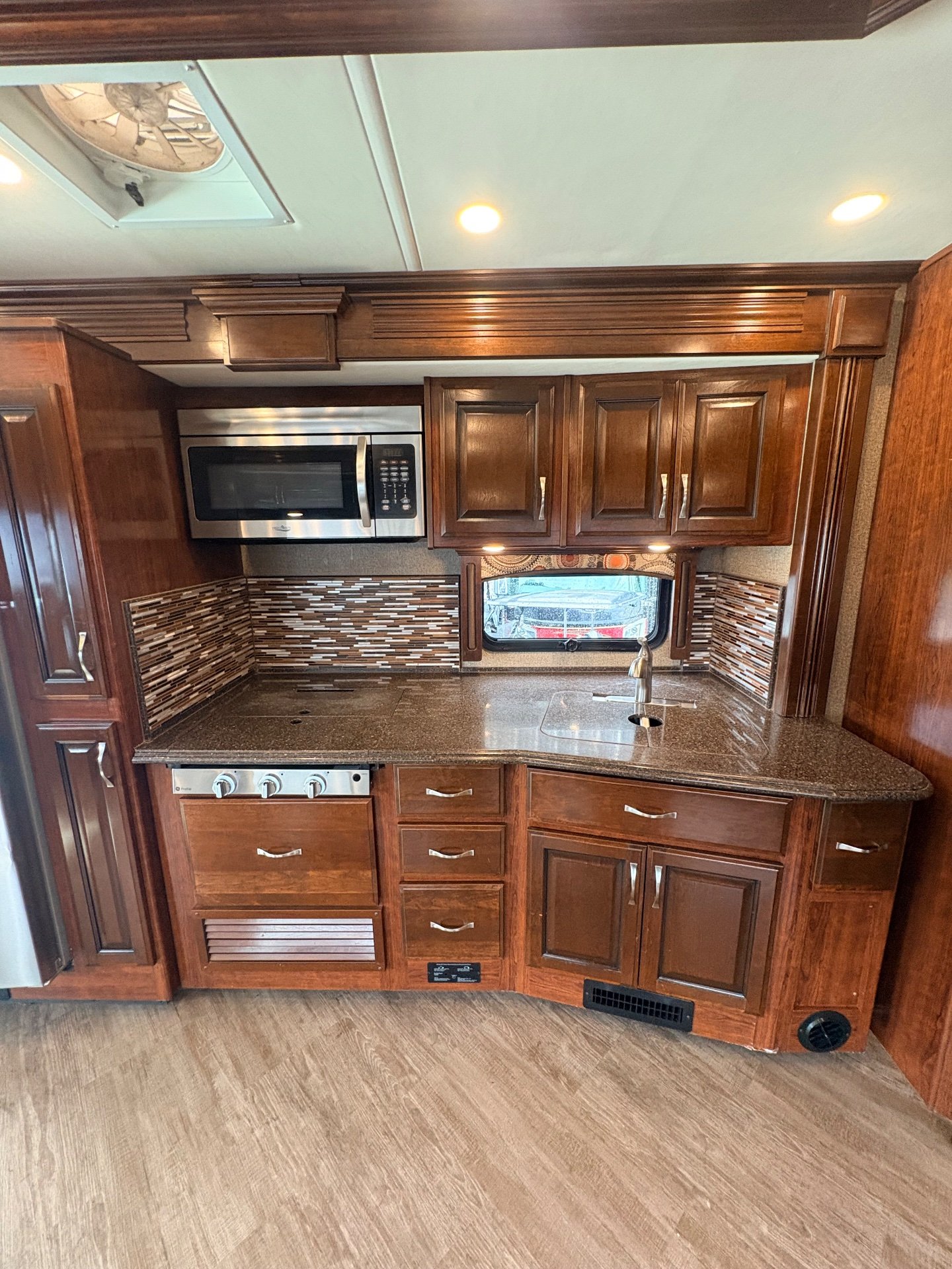 2019 Fleetwood Pace Arrow LXE 38N — Class A motorhome kitchen with microwave, sink, range, countertop, mosaic backsplash, and wood cabinetry