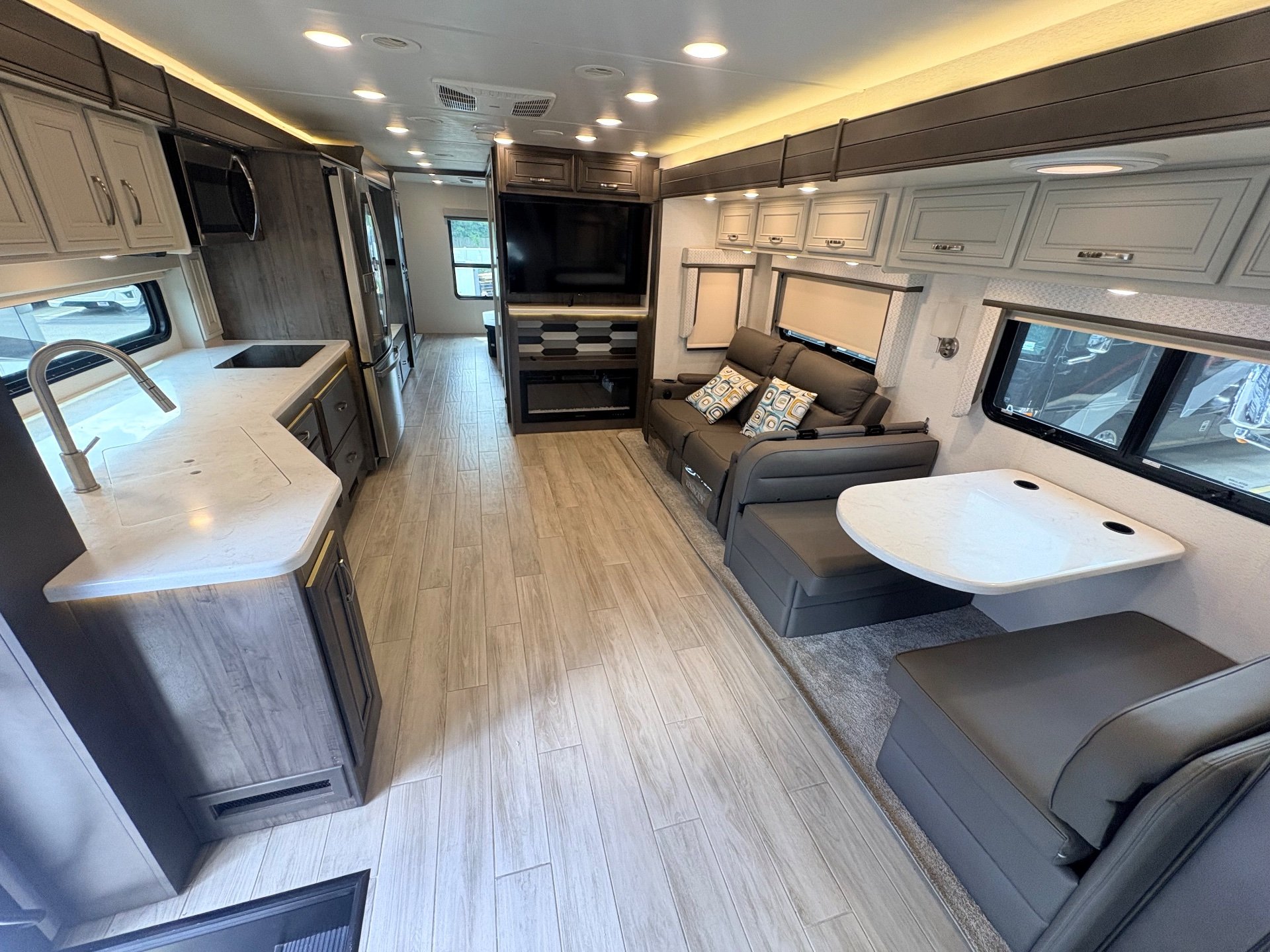2025 Entegra Coach Accolade XL 37L — Class C motorhome interior with lounge seating, dinette, television, and full kitchen extending along the opposite wall
