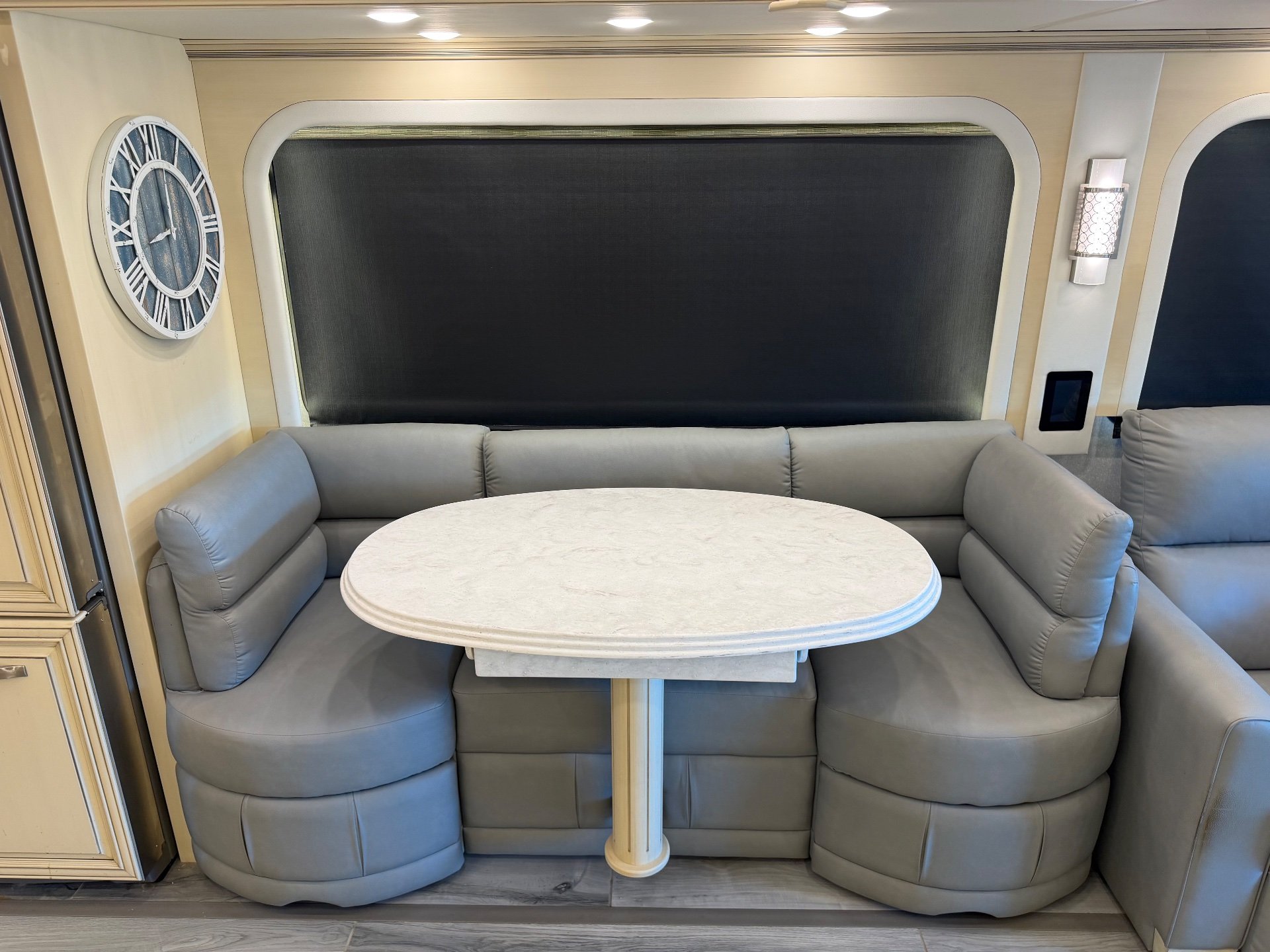 2022 Newmar Essex 4569 — Class A dinette with round table and curved upholstered booth seating beside a lounge chair
