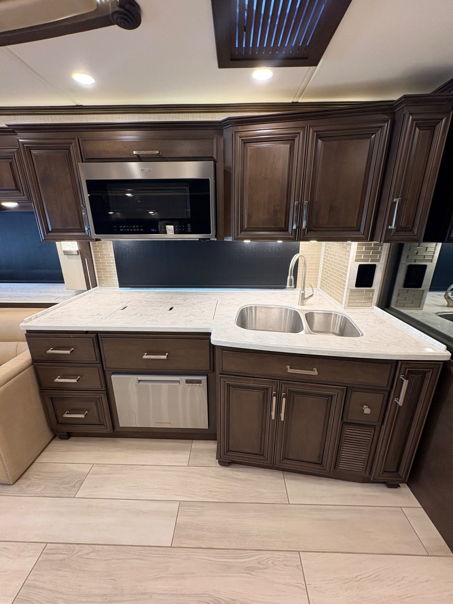 2023 Newmar London Aire 4579 — Motorhome kitchen with double sink, faucet, microwave, dishwasher, countertop, backsplash, and dark cabinetry