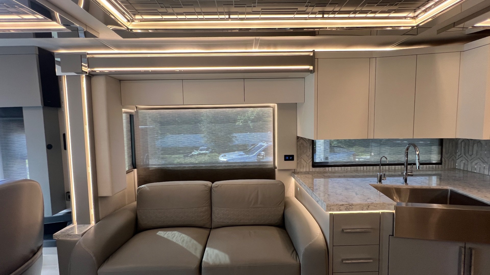 2025 Newmar King Aire 4558 — Kitchen counter with sink and cabinetry beside a two-seat sofa beneath large windows