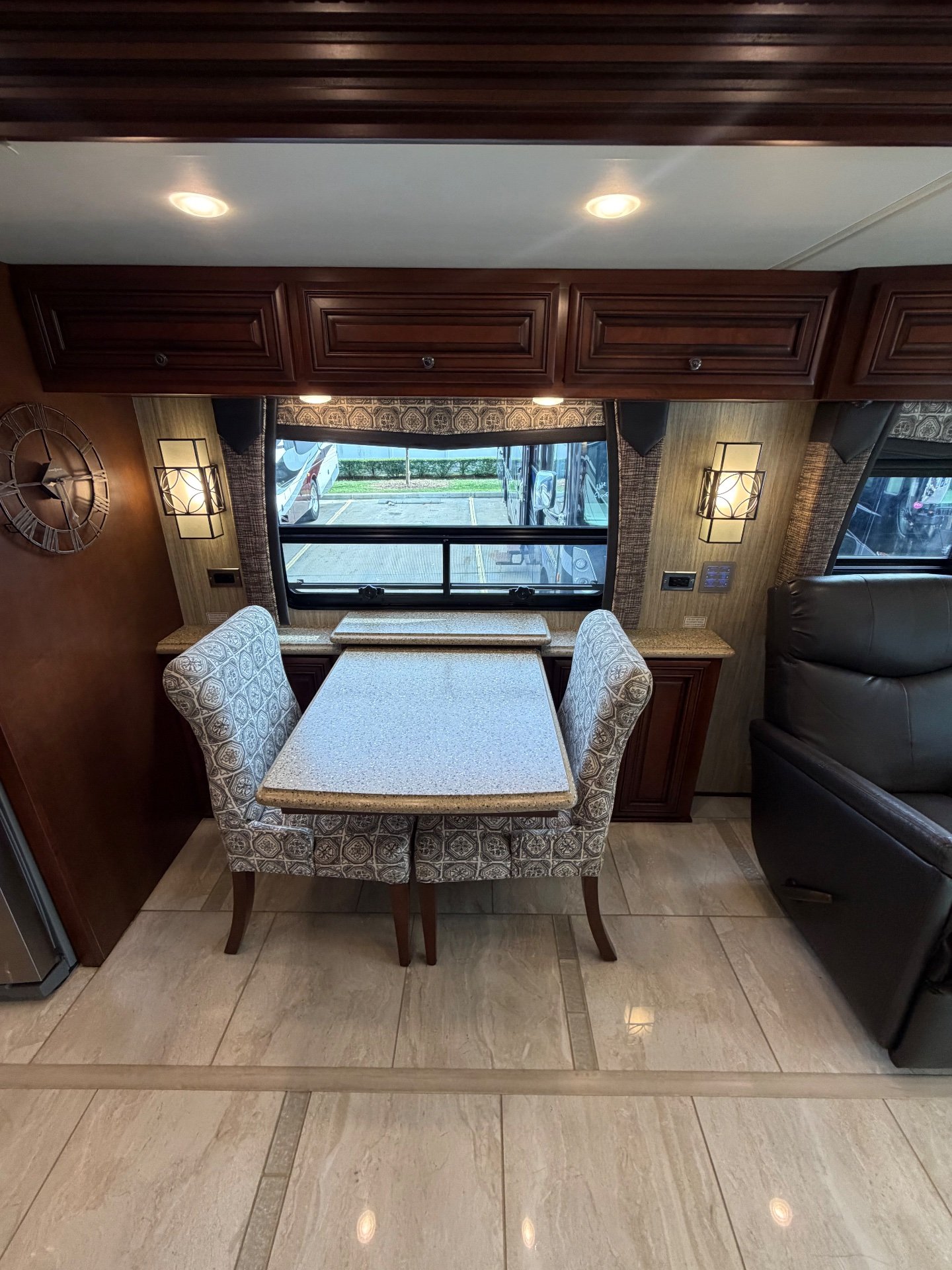 2017 Newmar Dutch Star 4369 — Dining table with four upholstered chairs beside a leather recliner, window, wall lights, and overhead cabinets