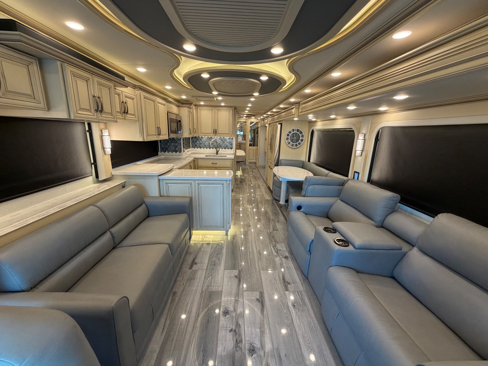 2022 Newmar Essex 4569 — Class A motorhome lounge with sofas and recliners, adjacent kitchen island, and rear dinette along a central aisle