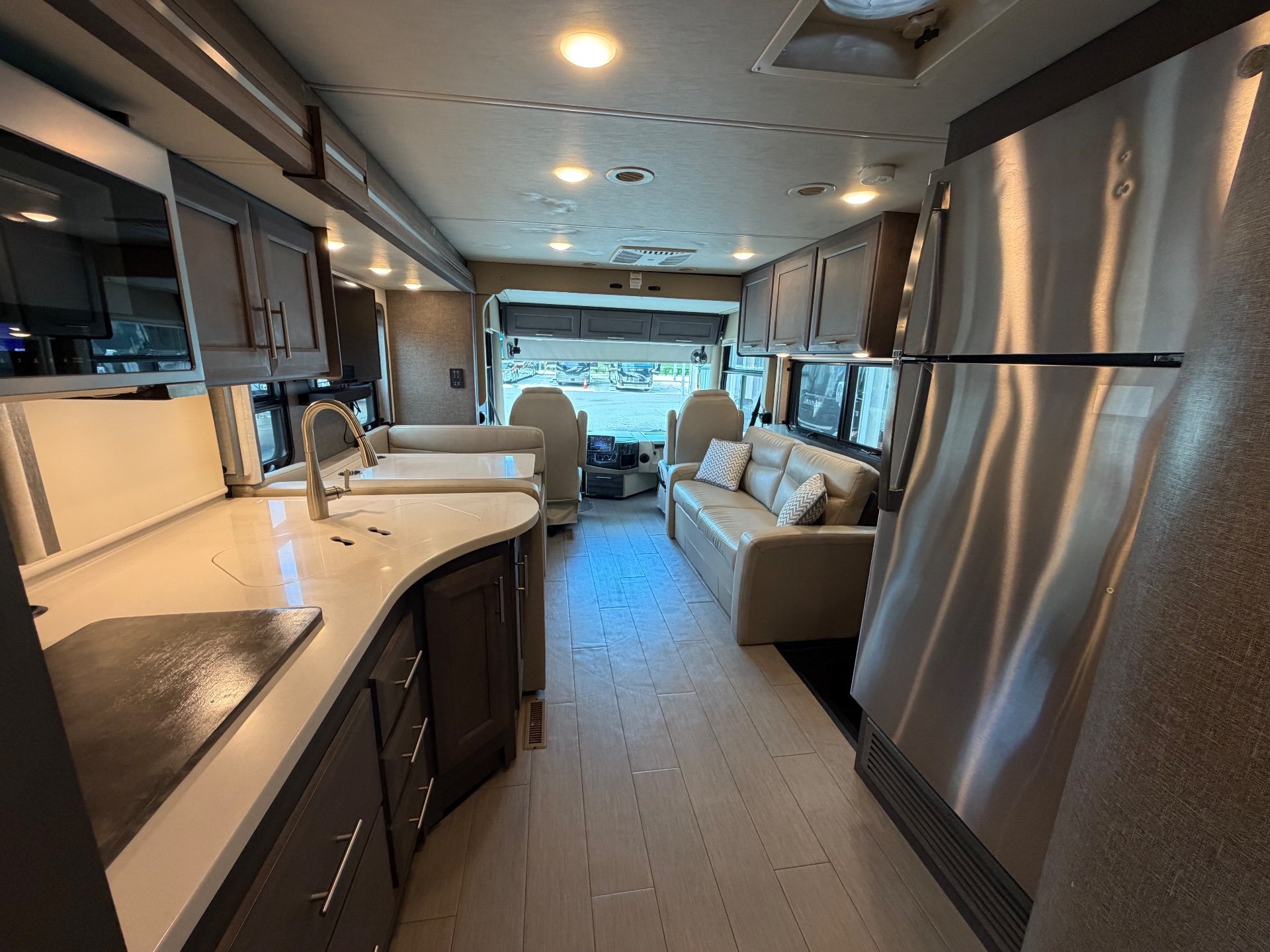 2022 Thor Motor Coach Palazzo 33.5 — Class A motorhome kitchen with curved counter, sink, refrigerator, sofa, and cockpit visible along the central aisle