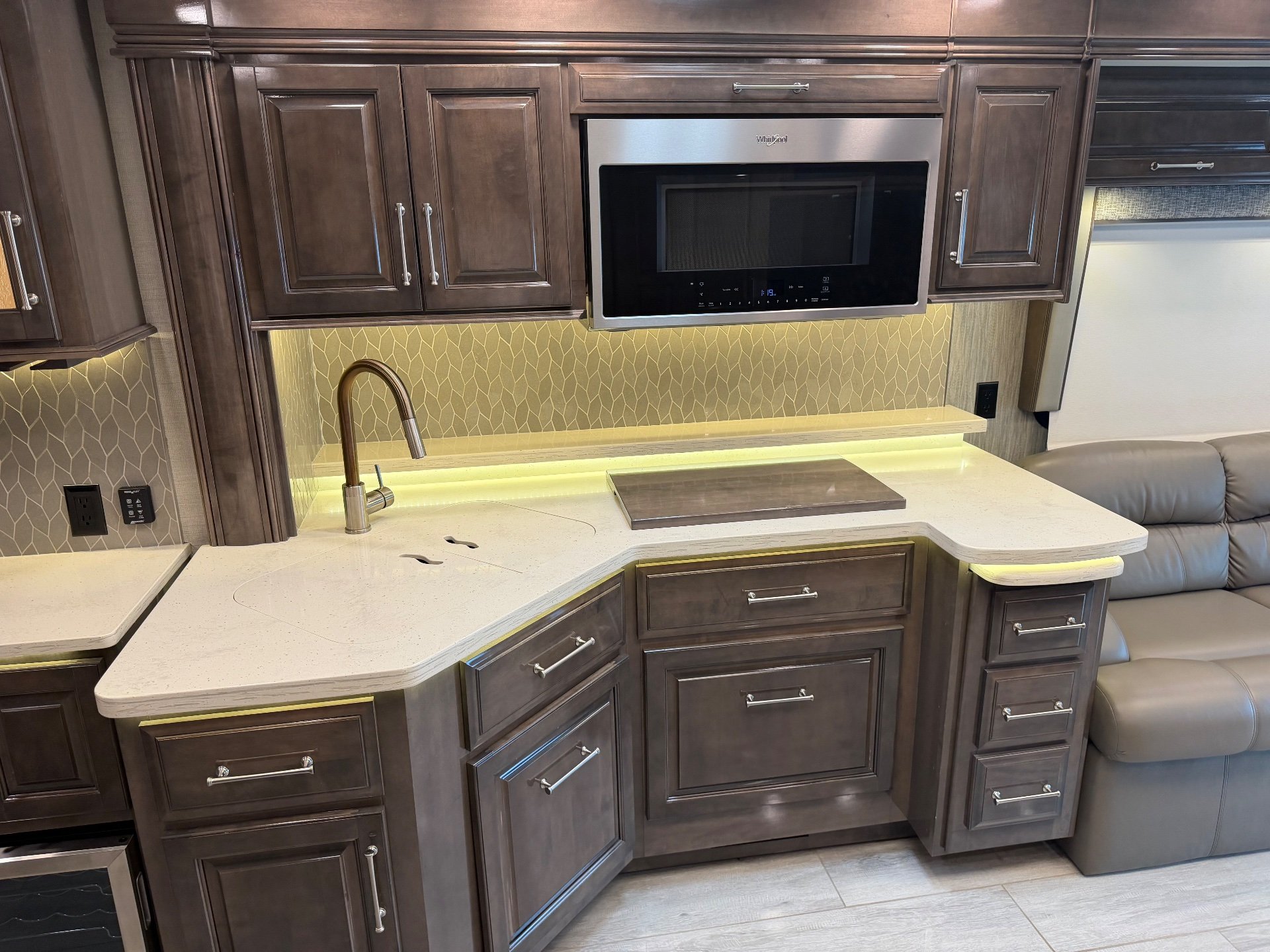 2020 Entegra Coach Aspire 44R — Kitchen counter with sink, cooktop cover, microwave, backsplash, and adjacent leather sofa