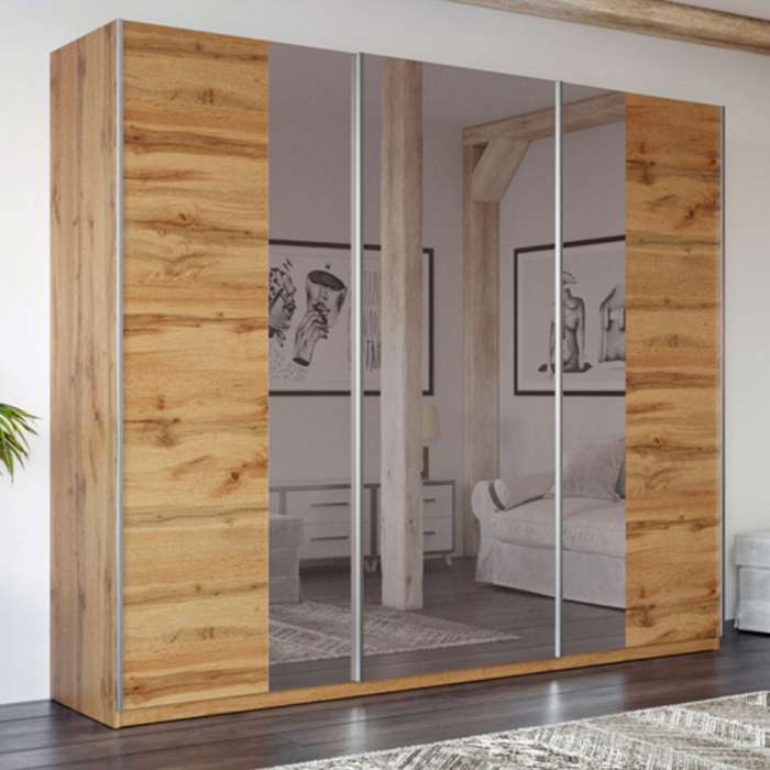 The sliding door wardrobe PRAGA 250cm oak wotan with mirrored doors in a bedroom.