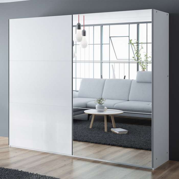 The sliding door wardrobe VIGO 250cm white with mirrored door in a room.