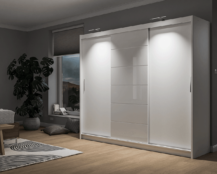 The sliding door wardrobe MALIBU white with LEDs in a cosy bedroom.