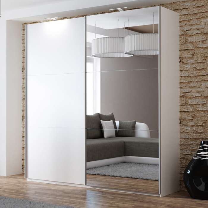 The sliding door wardrobe VIGO 200cm white with mirrored door and LED lights in a room.
