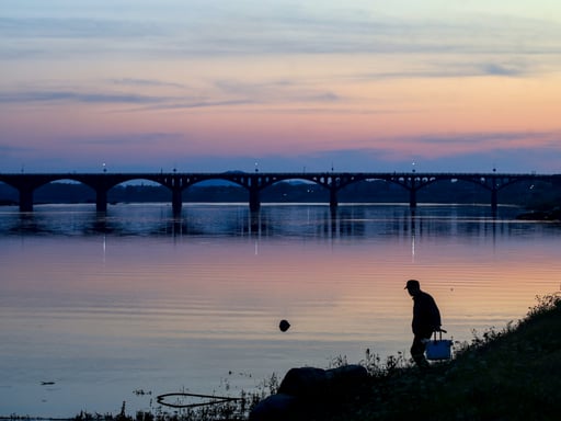 a man approaches the water, bucket in hand as the sun sets