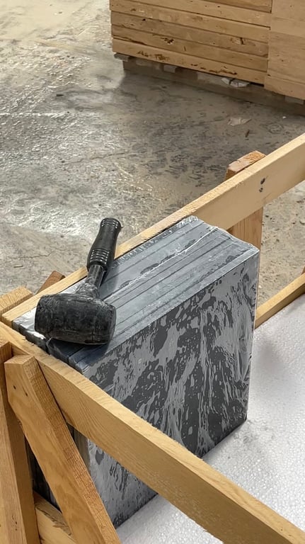 A rubber mallet resting on a banded stack of dark veined stone inside an open wooden crate.